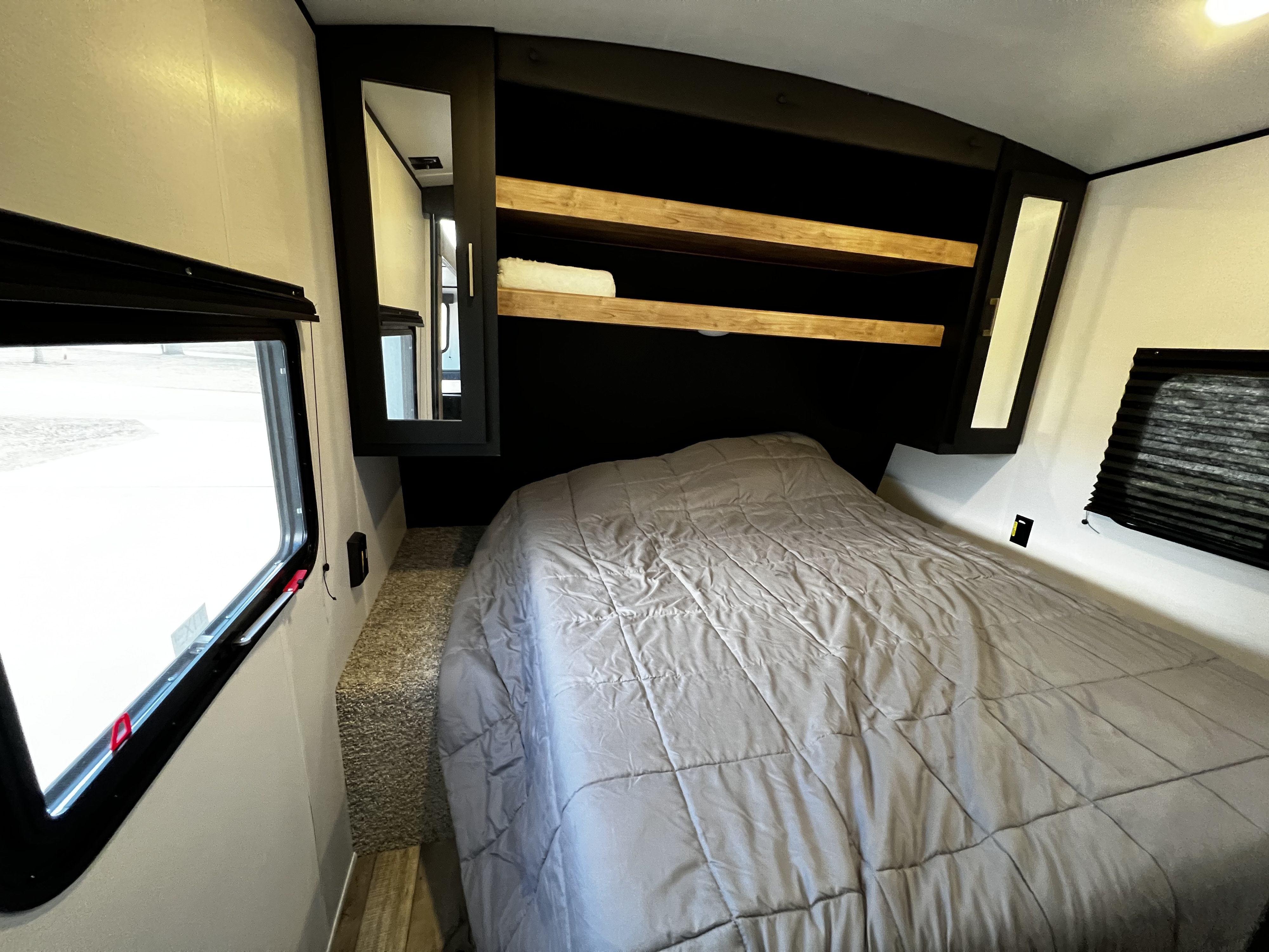Explore a cozy RV rental bedroom: bed with grey comforter, wood shelves, window, and mirrored storage.. Keystone RV Springdale 2022