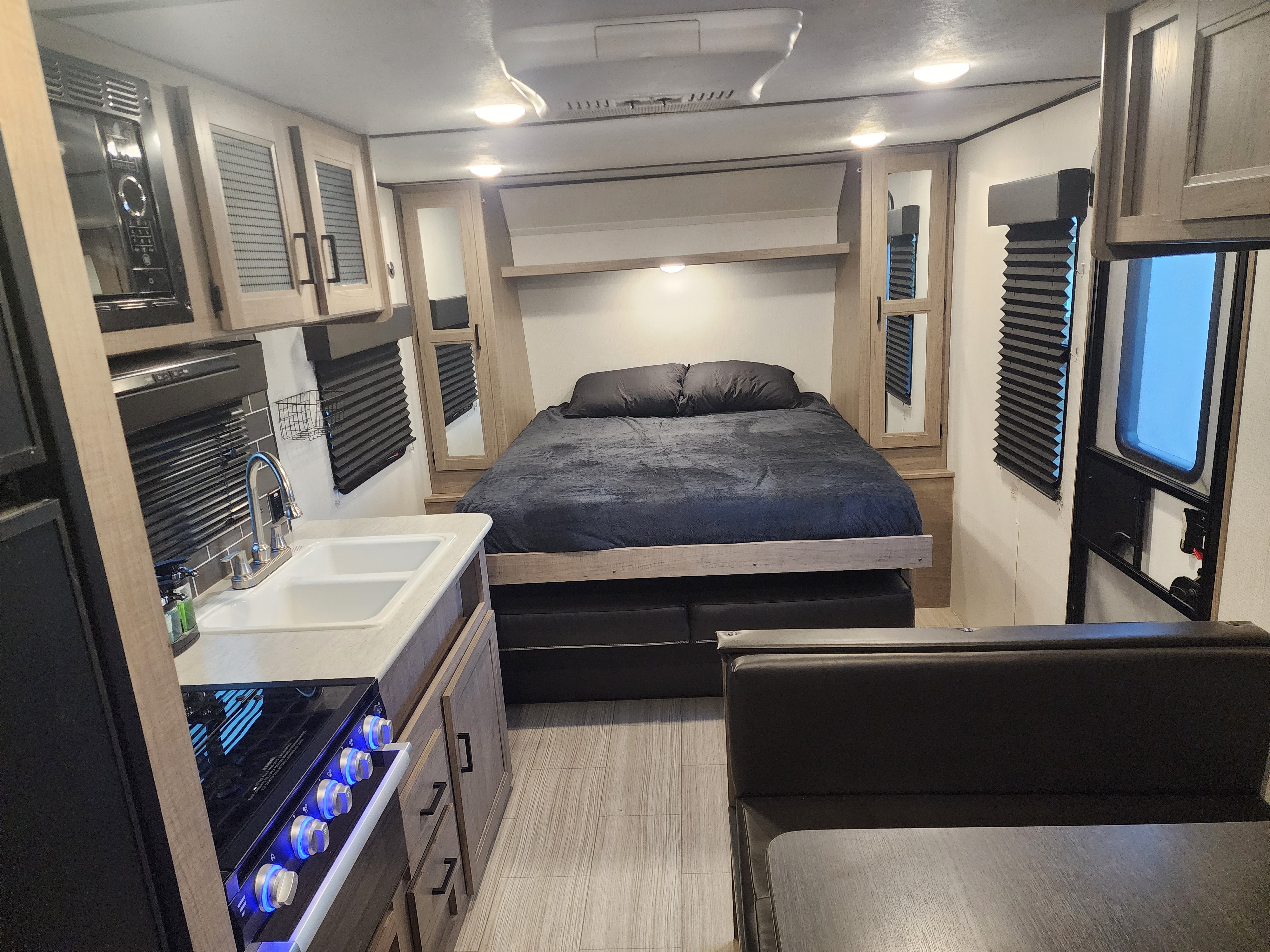 Modern rv rental interior: cozy bedroom, kitchen (microwave, sink, stove), and dining space.. Keystone RV Hideout 2022