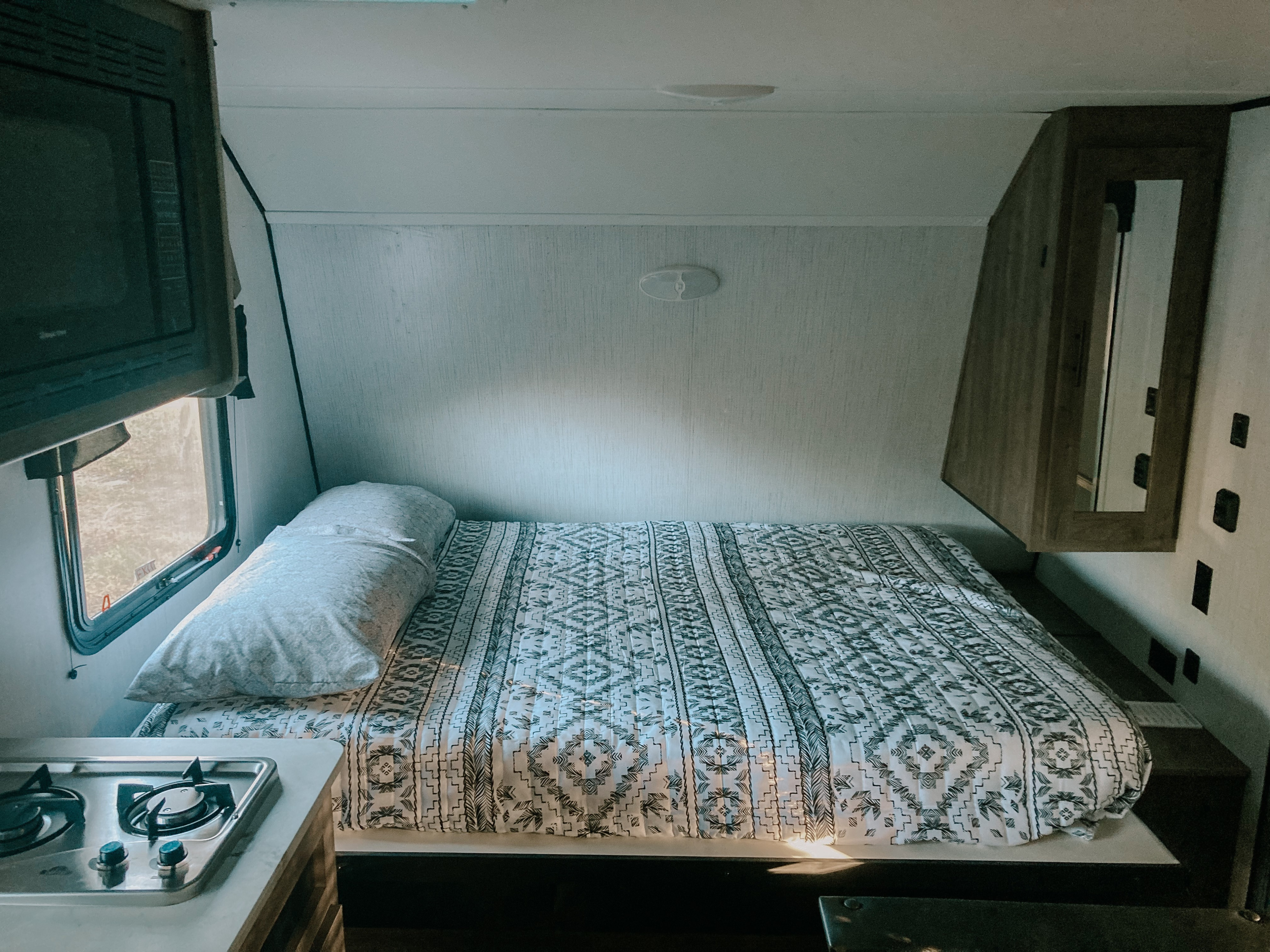 An inviting RV rental interior showcasing a patterned bed, compact kitchen with a stove and microwave, and a window.. Heartland RVs Pioneer Trail Blazer 2022