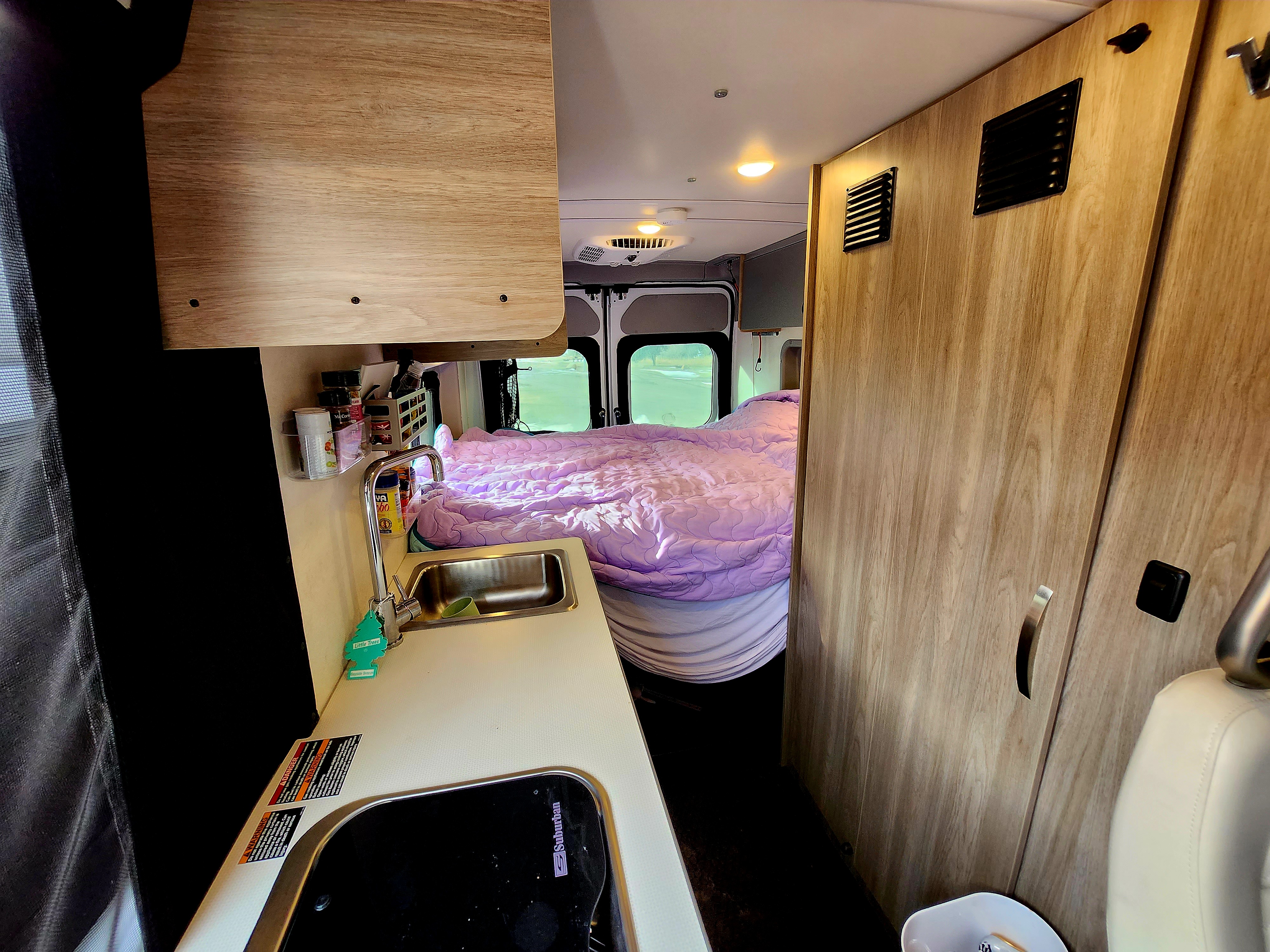 Cozy rv rental interior showing a compact kitchen with sink, stove, and a comfortable bed in the back of the camper van.. Winnebago Solis 2023