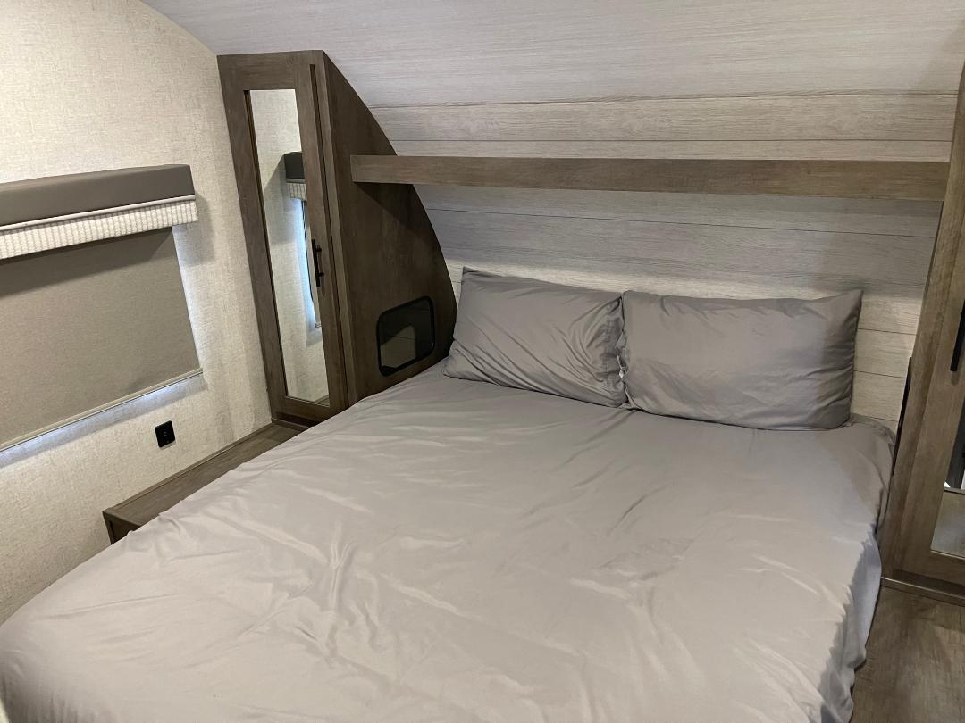 Comfortable RV rental bedroom with a gray bed, pillows, built-in storage, and a window with a shade.. Forest River Salem Cruise Lite 2022