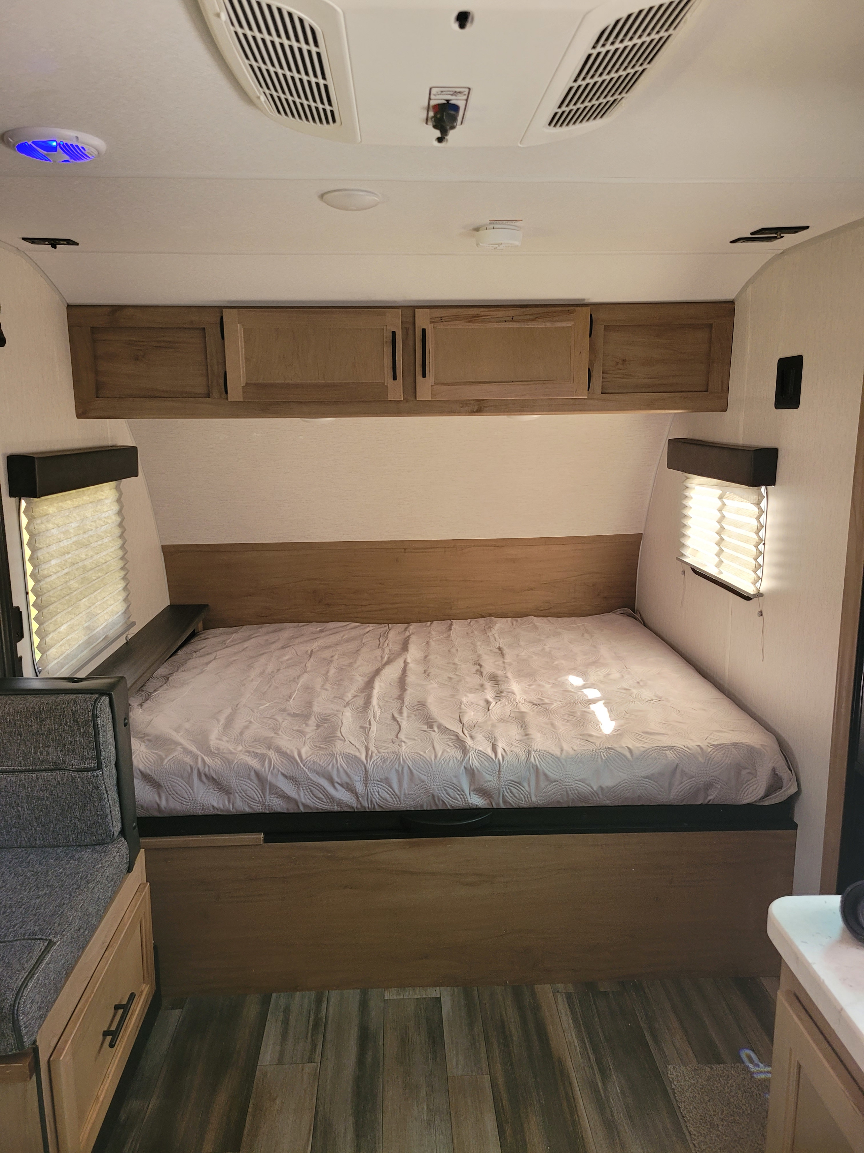 Cozy RV rental interior featuring a comfortable bed, overhead cabinets, and windows, ideal for travel and camping.. forest river wolf pup 2023