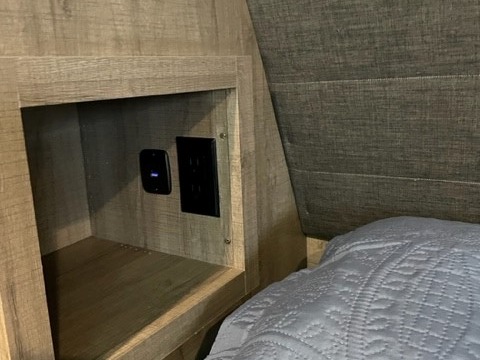 RV rental convenience: Built-in shelf with power outlets & USB charging in a cozy bedroom. Grey headboard and bed visible.. Grand Design Imagine 2022