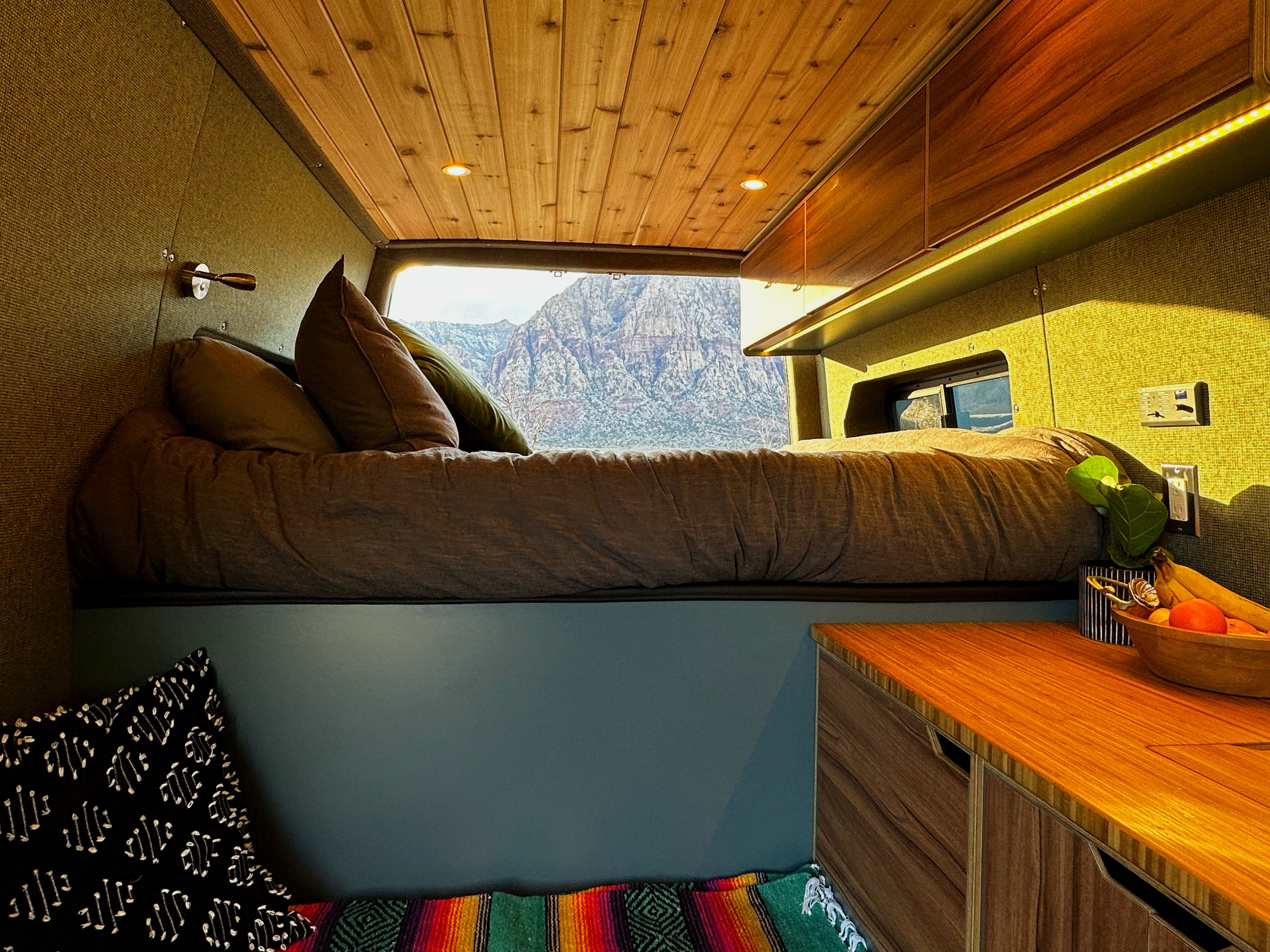 Relax in this RV rental's cozy interior, featuring a comfy bed, warm wood ceiling, and stunning mountain views from the back.. Mercedes-Benz Sprinter 419 LWB High Roof 2021