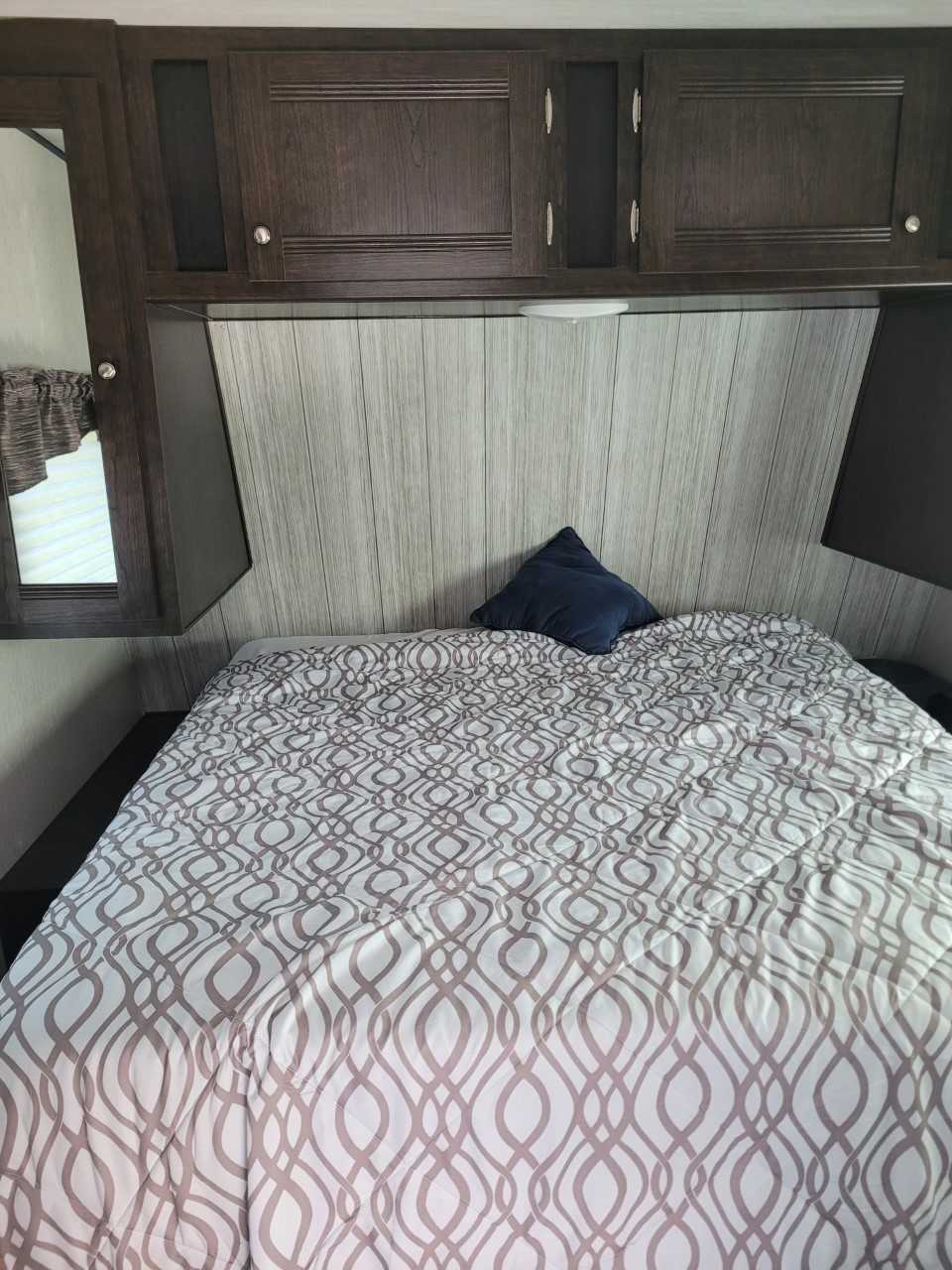 Cozy RV rental bedroom with patterned bedspread, overhead cabinets, and built-in mirror.. Heartland RVs Pioneer 2020