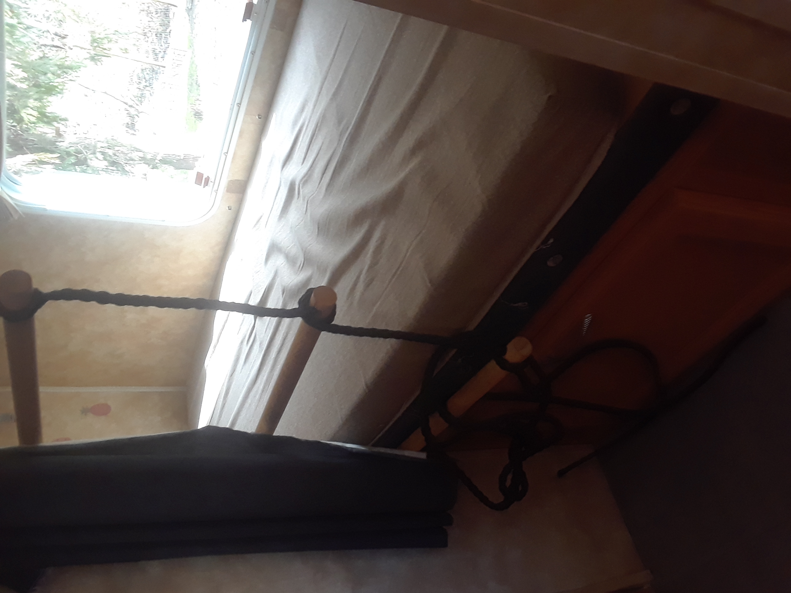 Inside an RV rental: a bunk bed with a mattress, window, dark curtain, and a unique rope ladder for access.. Coachmen Other 2006