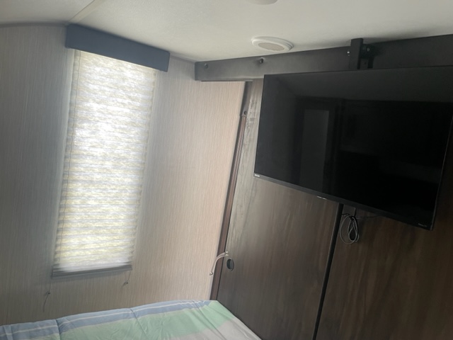 Inside this RV rental bedroom: a bright window with pleated blinds and a wall-mounted TV.. Forest River Cherokee Alpha Wolf 2021