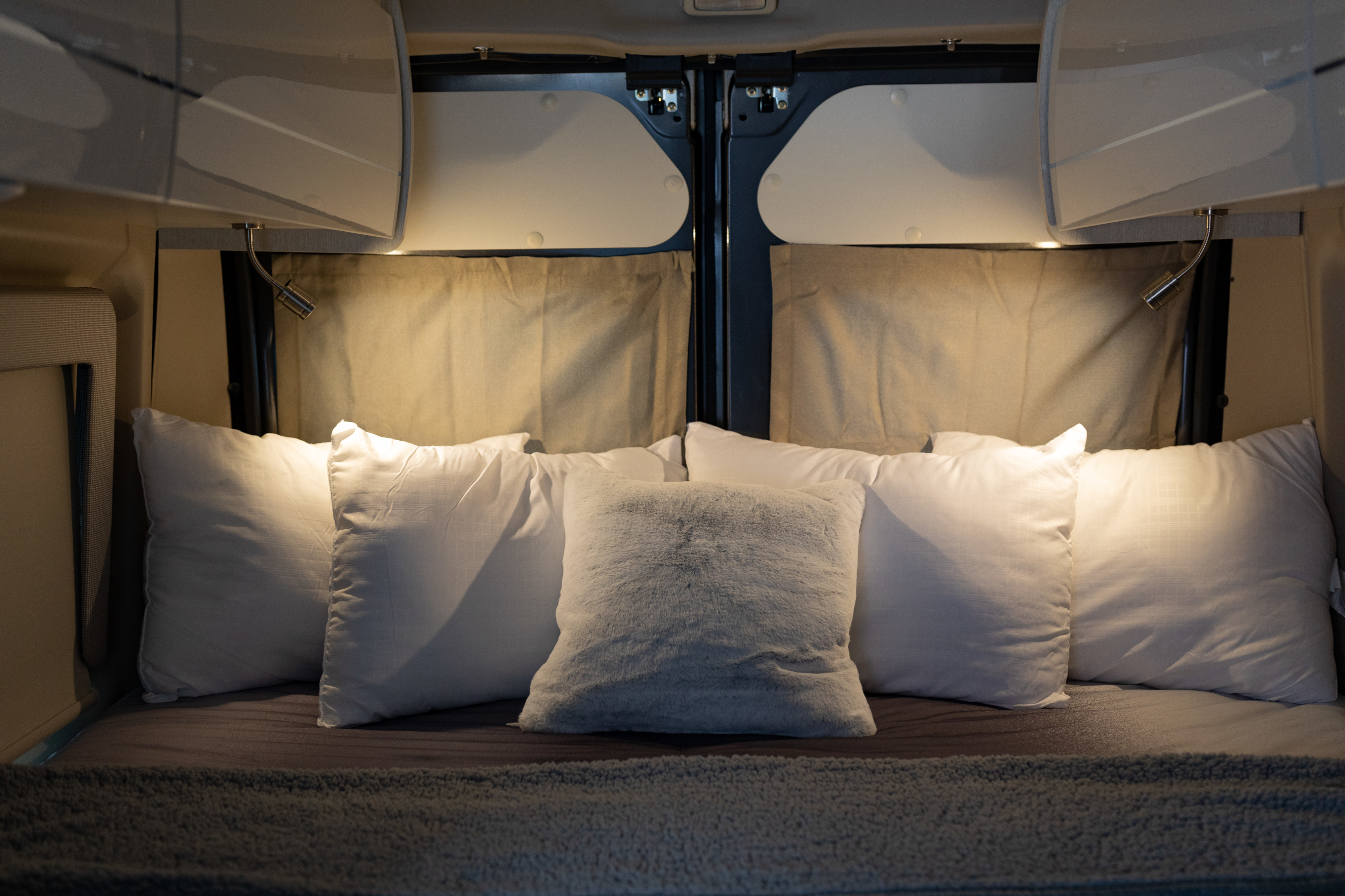 Plush pillows and reading lights create a cozy RV rental bedroom. Overhead cabinets complete this comfortable, well-lit space.. Thor Tellaro 2023