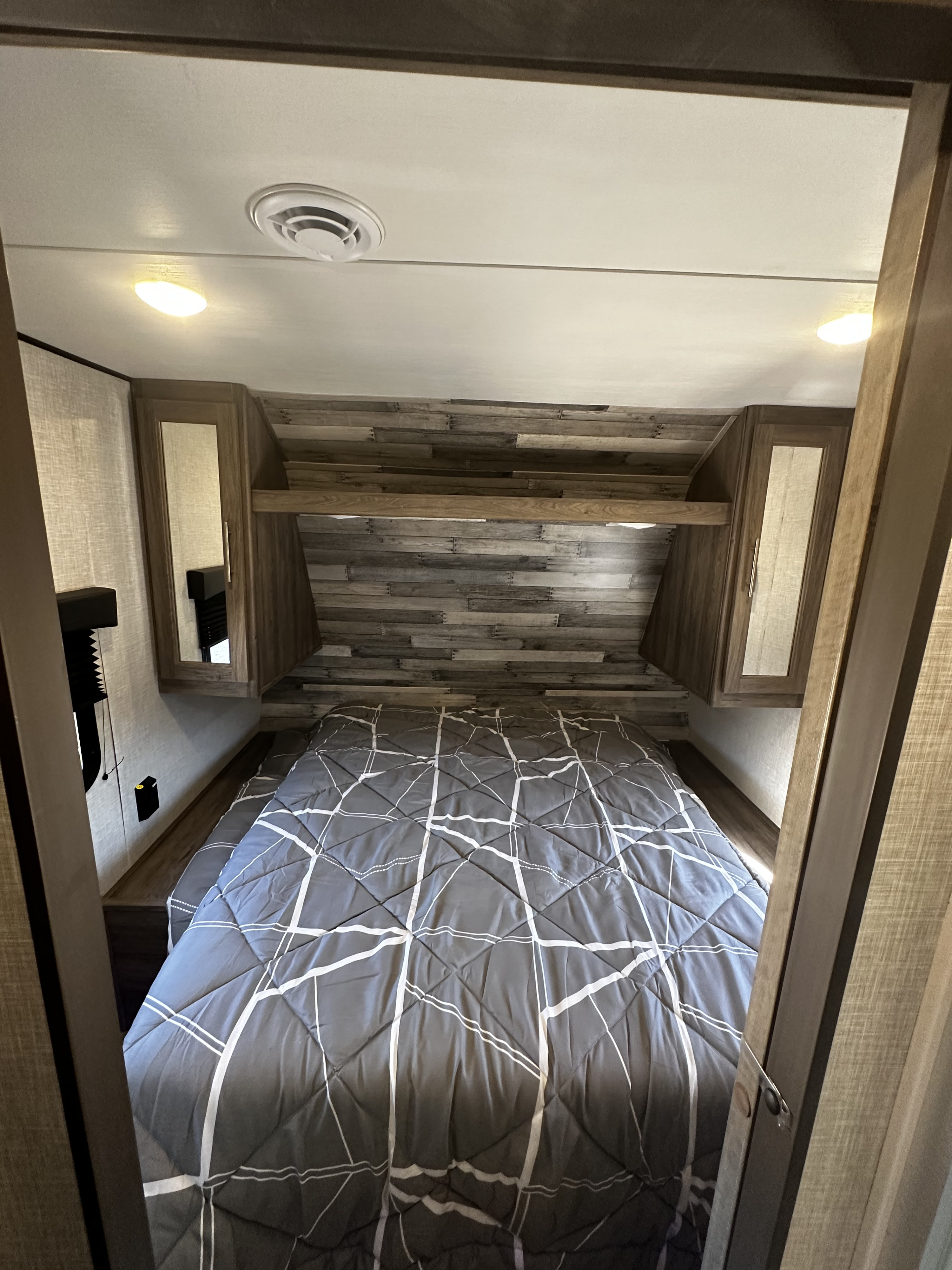 RV rental bedroom with a neatly made bed, overhead cabinets, and wood-paneled walls, offering a cozy retreat.. Crossroads Zinger 2023