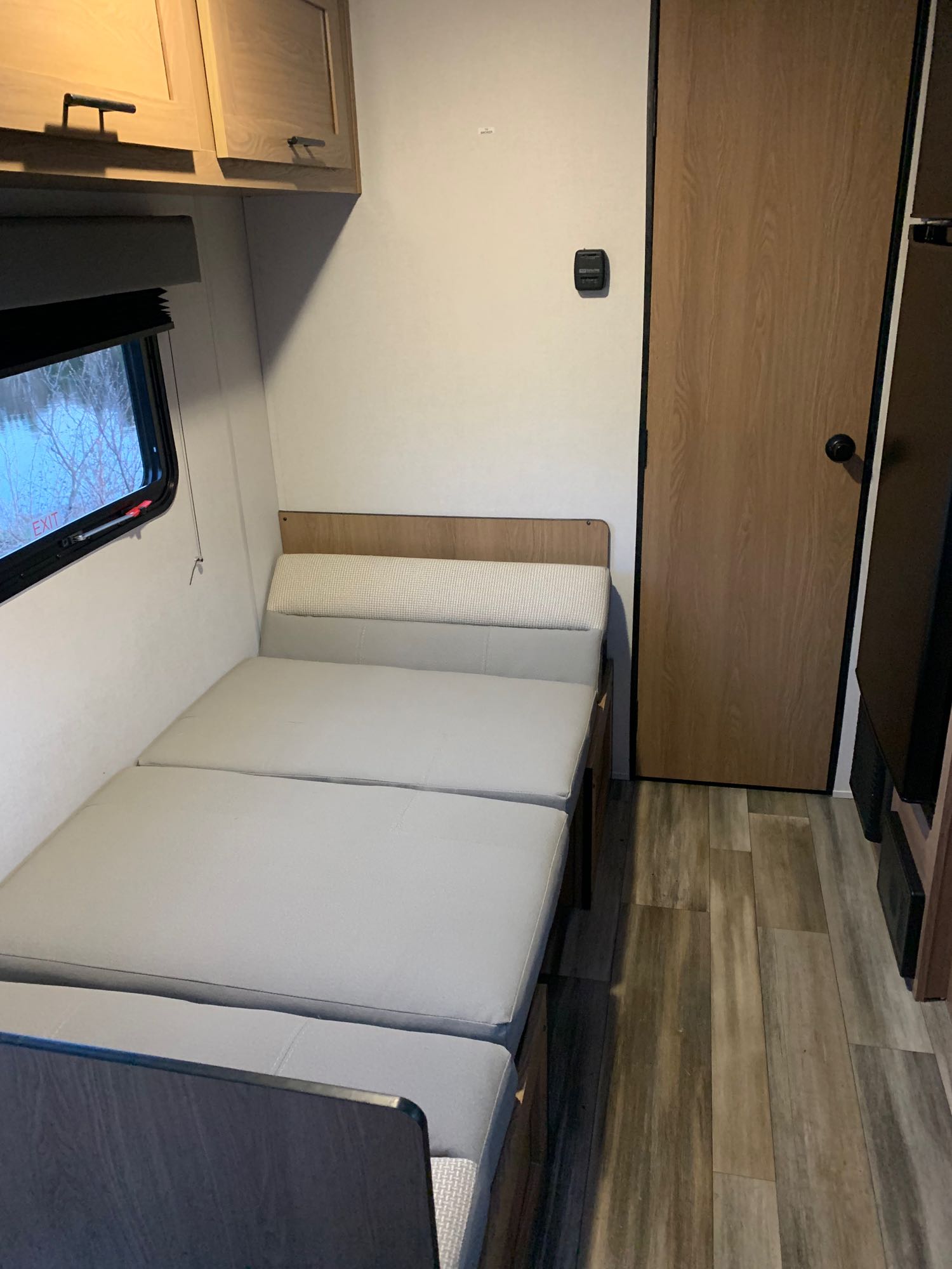 RV rental interior: window, light wood cabinets, convertible dinette bed, wood-look floor, and door with thermostat.. Avenger LT 2022