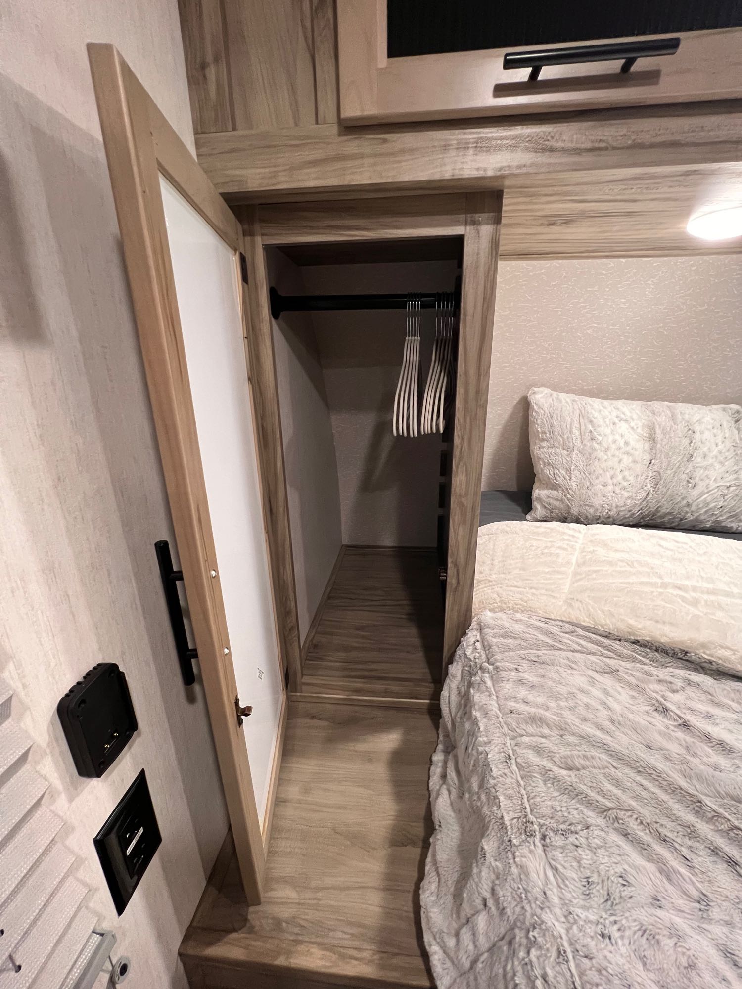 RV rental bedroom with a cozy, light-colored bed and an open closet, showing empty hangers, in a modern interior.. Forest River Cherokee 2021