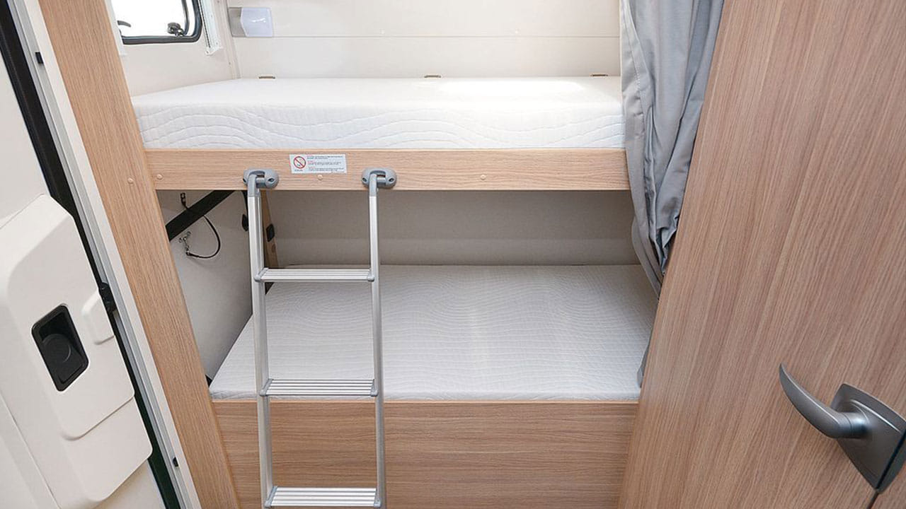 This RV rental features a cozy sleeping area with two bunk beds, a ladder, and wooden finishes inside the camper.. Sunlight A72 2023