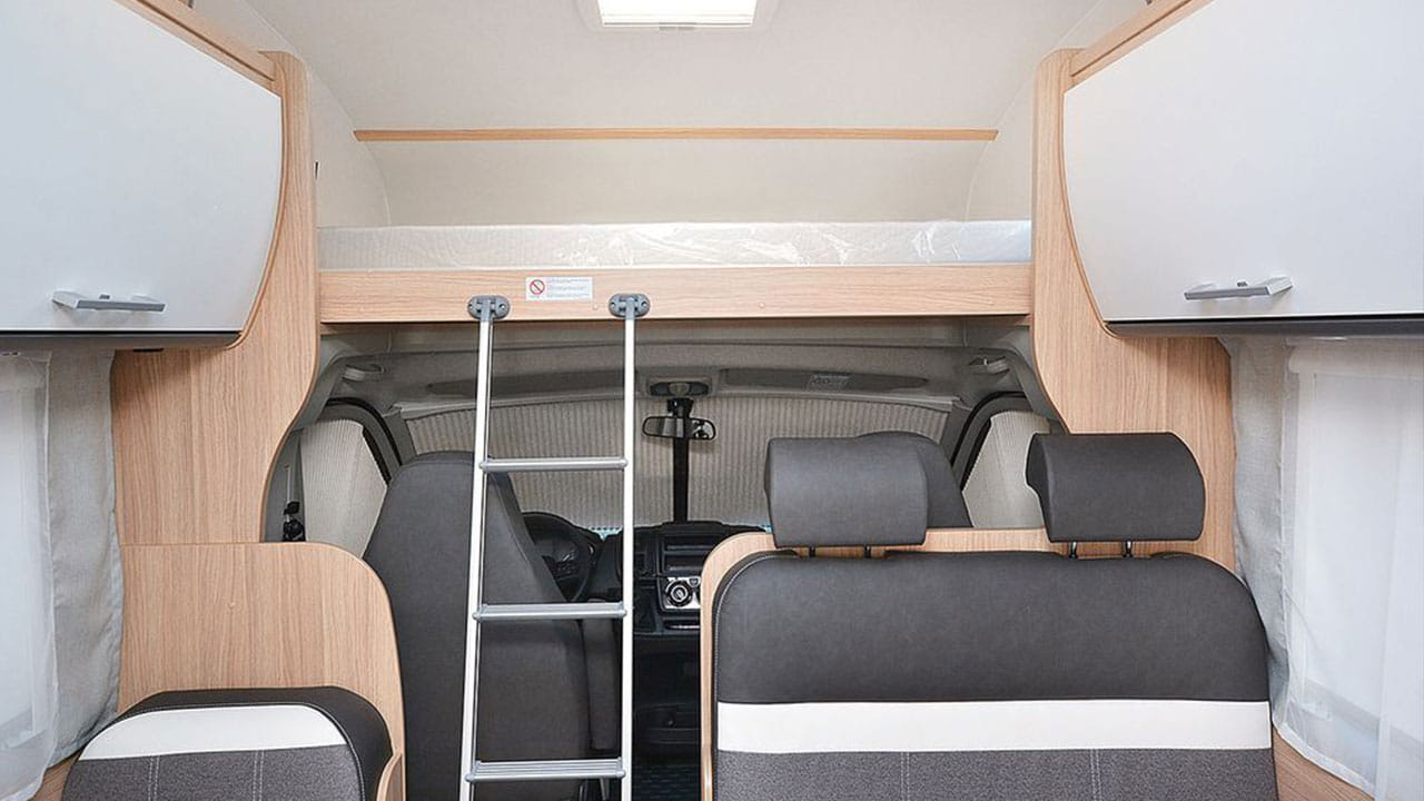 Spacious RV rental interior with an over-cab bunk bed, ladder, overhead cabinets, and driver's area.. Sunlight A72 2023