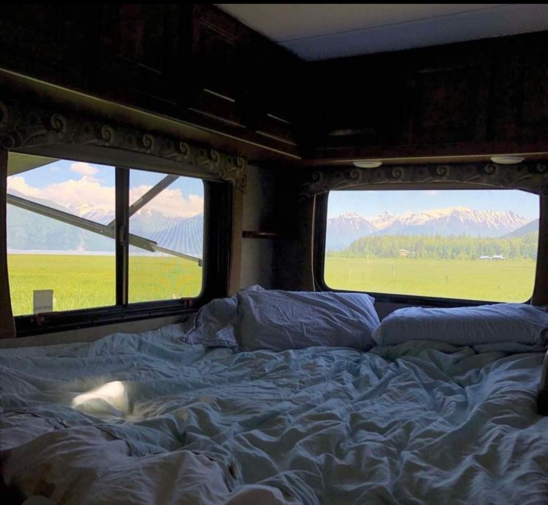 Cozy RV rental bedroom with a stunning view of green fields and snow-capped mountains. Perfect for nature lovers!. Forest River Sunseeker 2016