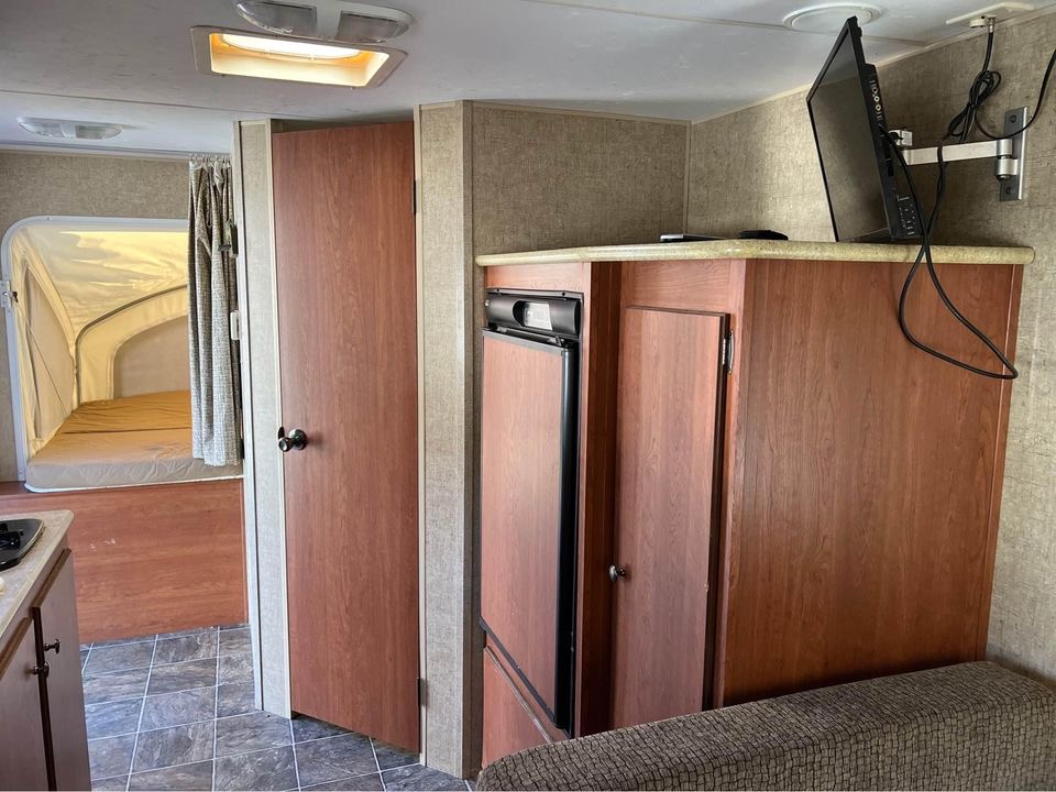 RV rental interior: cozy pop-out bed, compact fridge, and TV. A functional living space for your next adventure.. FABRIQUE KZRV Sportsmen Classic 2014