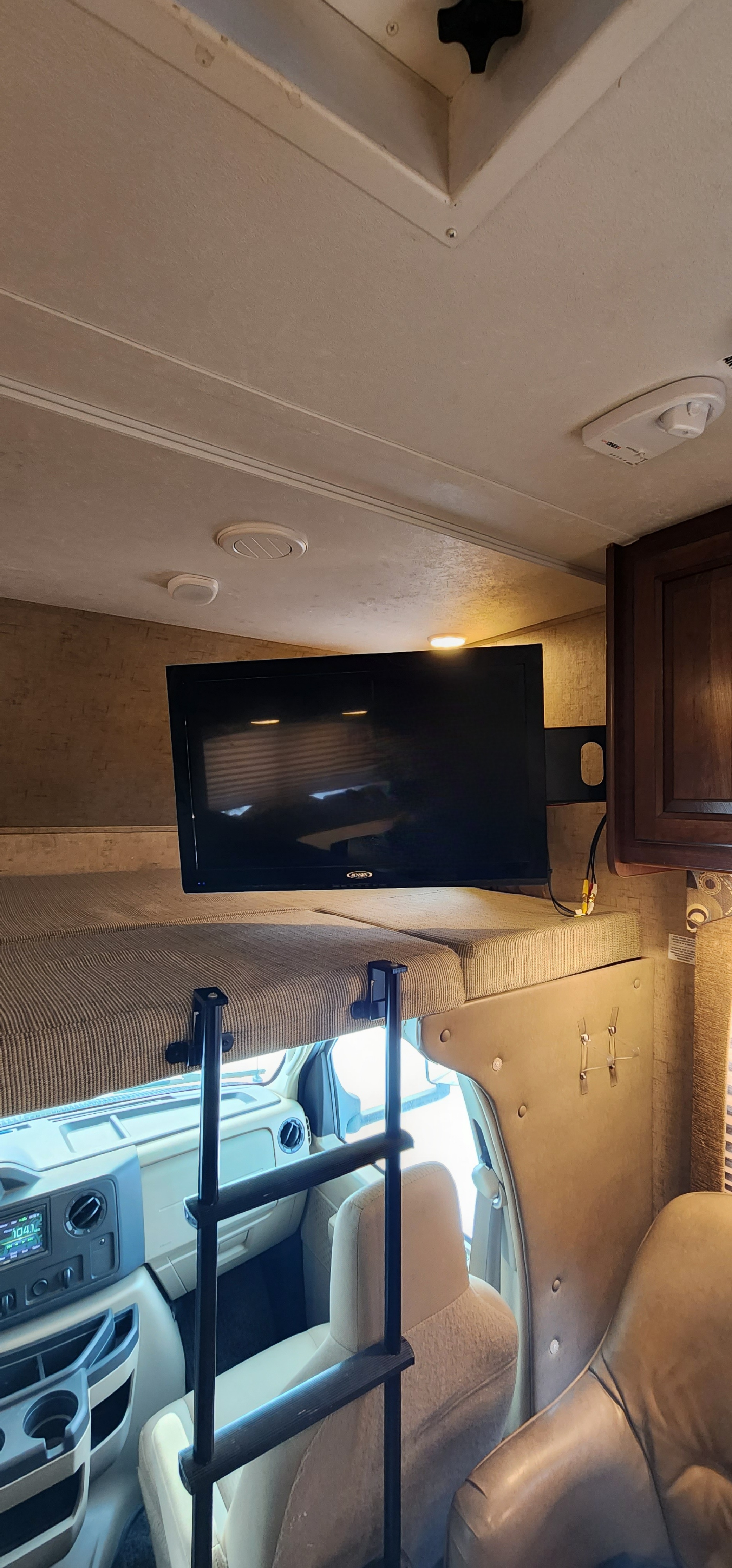 Inside an RV rental, showing the front cab, an overhead bunk bed with a ladder, and a wall-mounted TV.. Forest River Sunseeker 2016