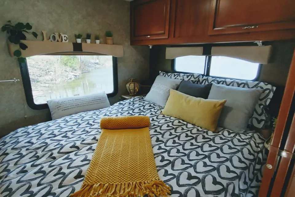 Experience comfort in this cozy RV rental bedroom. Features a heart-patterned bed, throw, and scenic window views.. Fleetwood Storm 2014