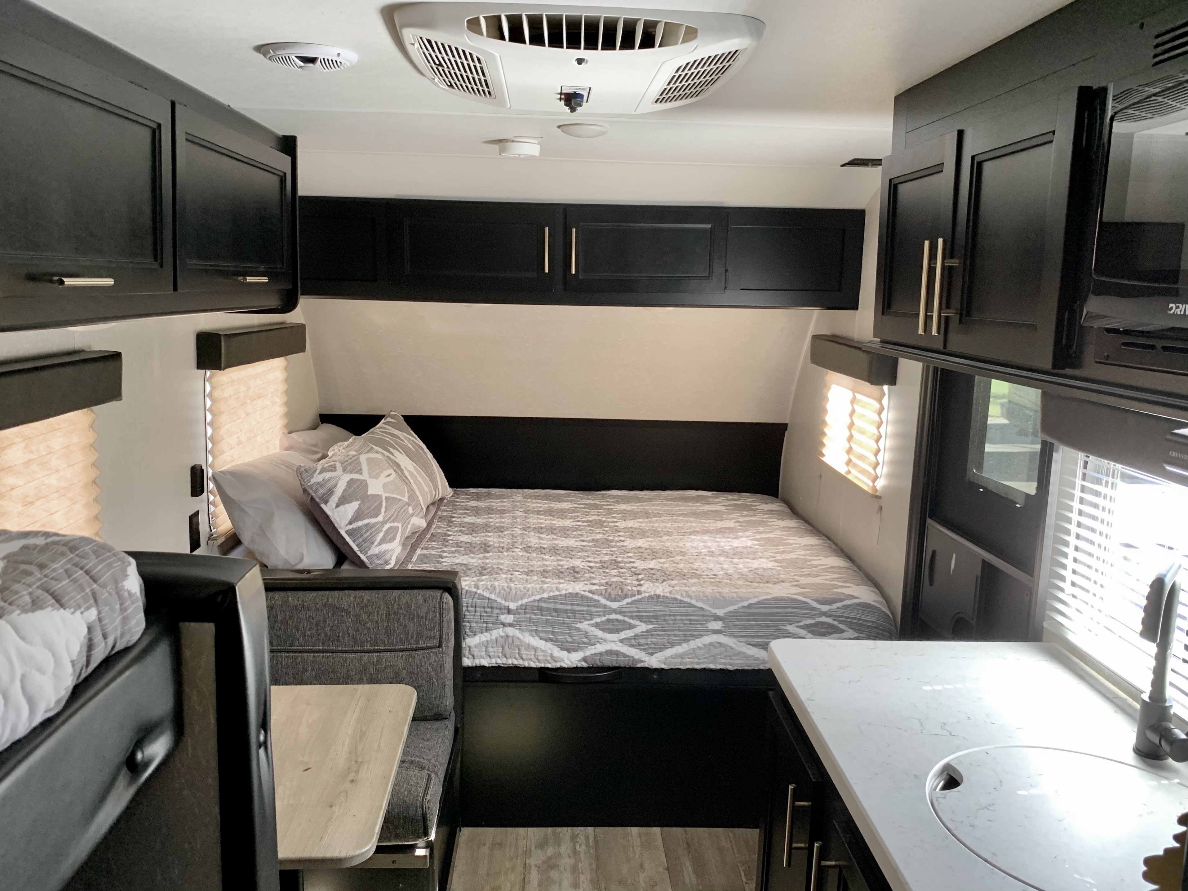 Bright RV rental interior shows a bed with storage, modern black cabinets, dining nook, and kitchen sink. Compact and functional mobile living.. Forest River Cherokee Wolf Pup 2021