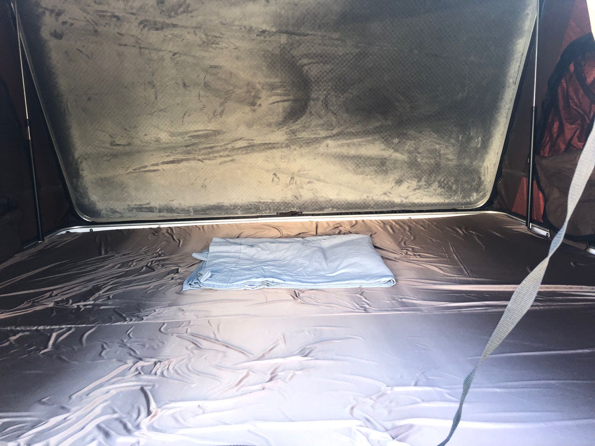 Inside an RV rental rooftop tent. A dark mattress and folded light blue bedding await, ready for a comfortable night.. Toyota Other 2008