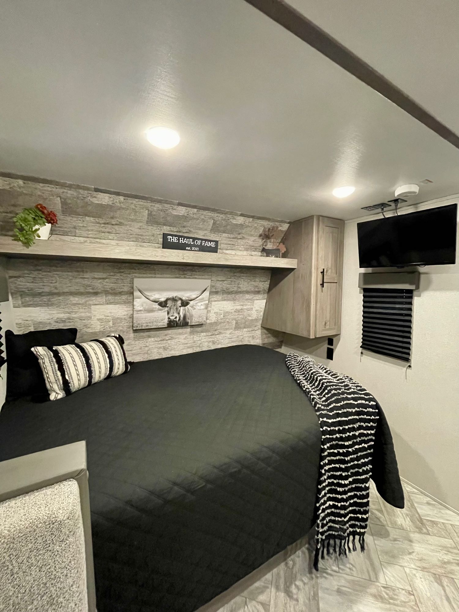 Cozy RV rental bedroom featuring a comfy bed, wall-mounted TV, and rustic wood-paneled walls.. Keystone Springdale 2021