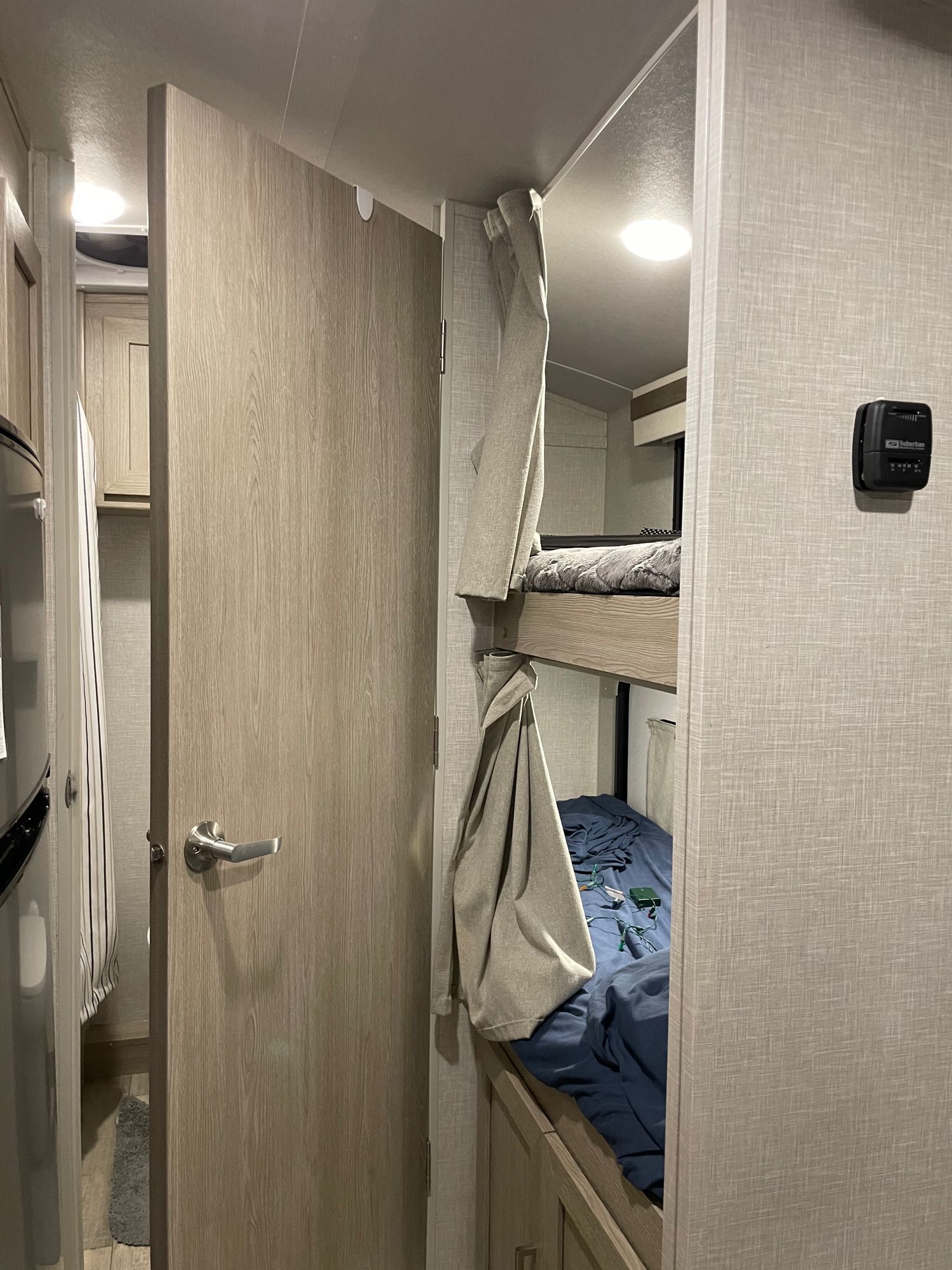 Cozy RV rental interior featuring bunk beds with privacy curtains, a partially open door to a bathroom, and a thermostat.. Forest River Rockwood Geo Pro 2022