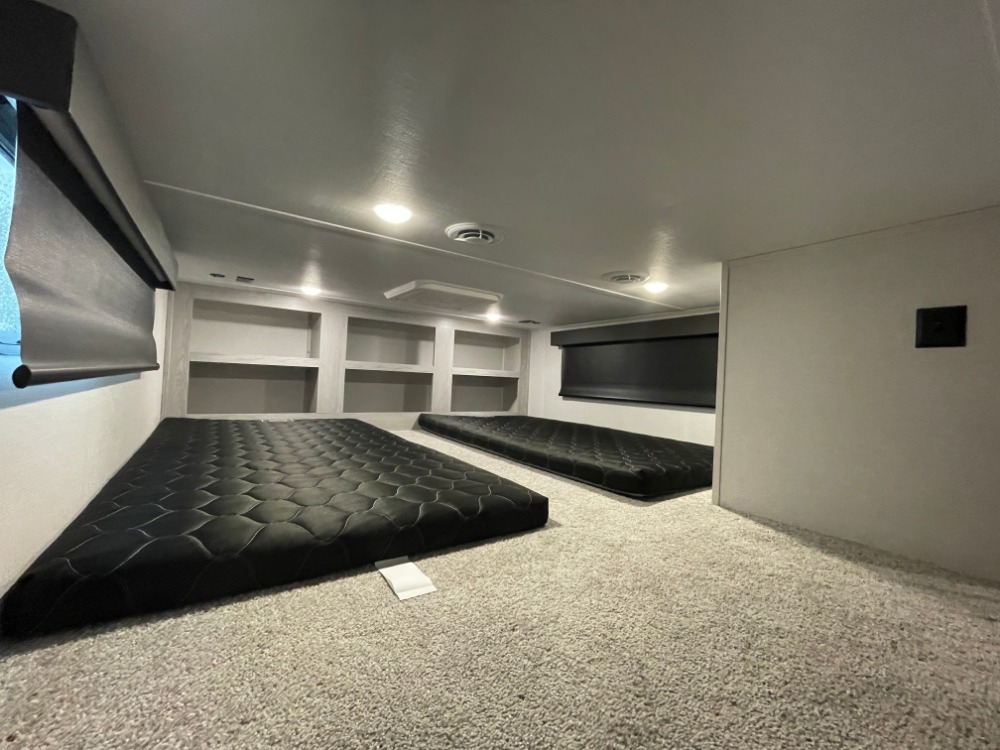 RV rental sleeping area featuring two low-profile black mattresses, built-in storage shelves, and soft carpet. Ideal for family comfort.. Keystone RV Montana High Country 2023