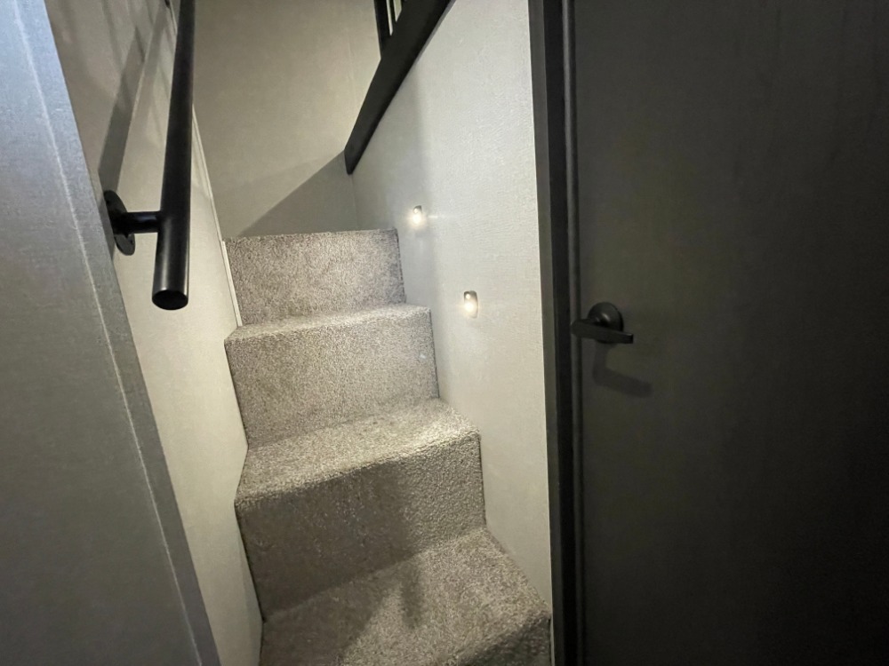 Carpeted stairs with handrail, step lights, and dark door in a modern RV rental. Compact and functional design.. Keystone RV Montana High Country 2023