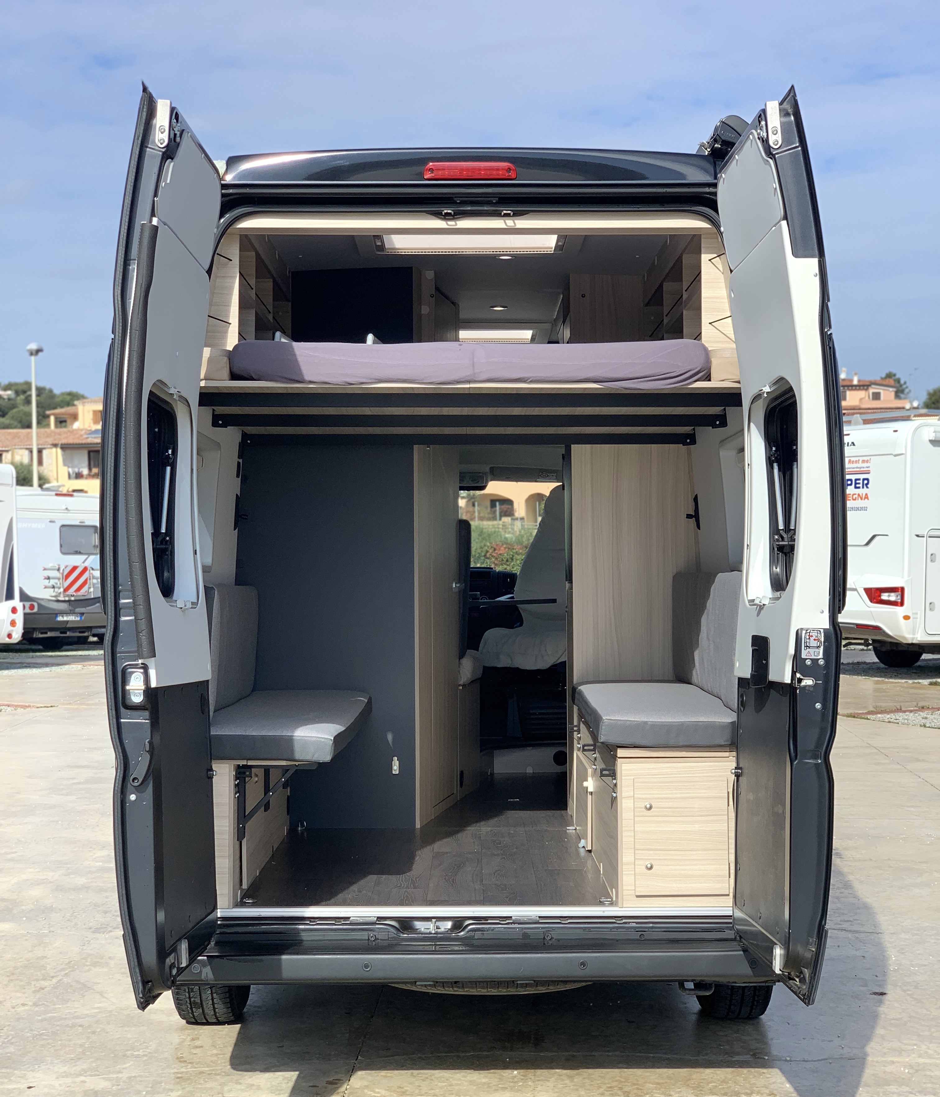 RV rental's open rear doors show a two-tier interior: an elevated bed and a customizable lower living space.. SunLiving V 65 XL 2022