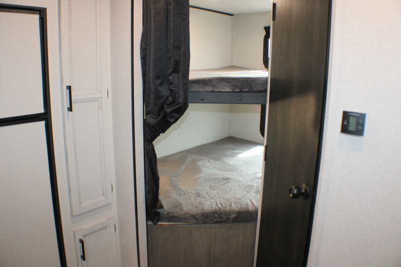 View of the bunk beds inside an RV rental. Two stacked beds are visible beyond a privacy curtain, with cabinetry to the left.. Open Range Open Range 2022