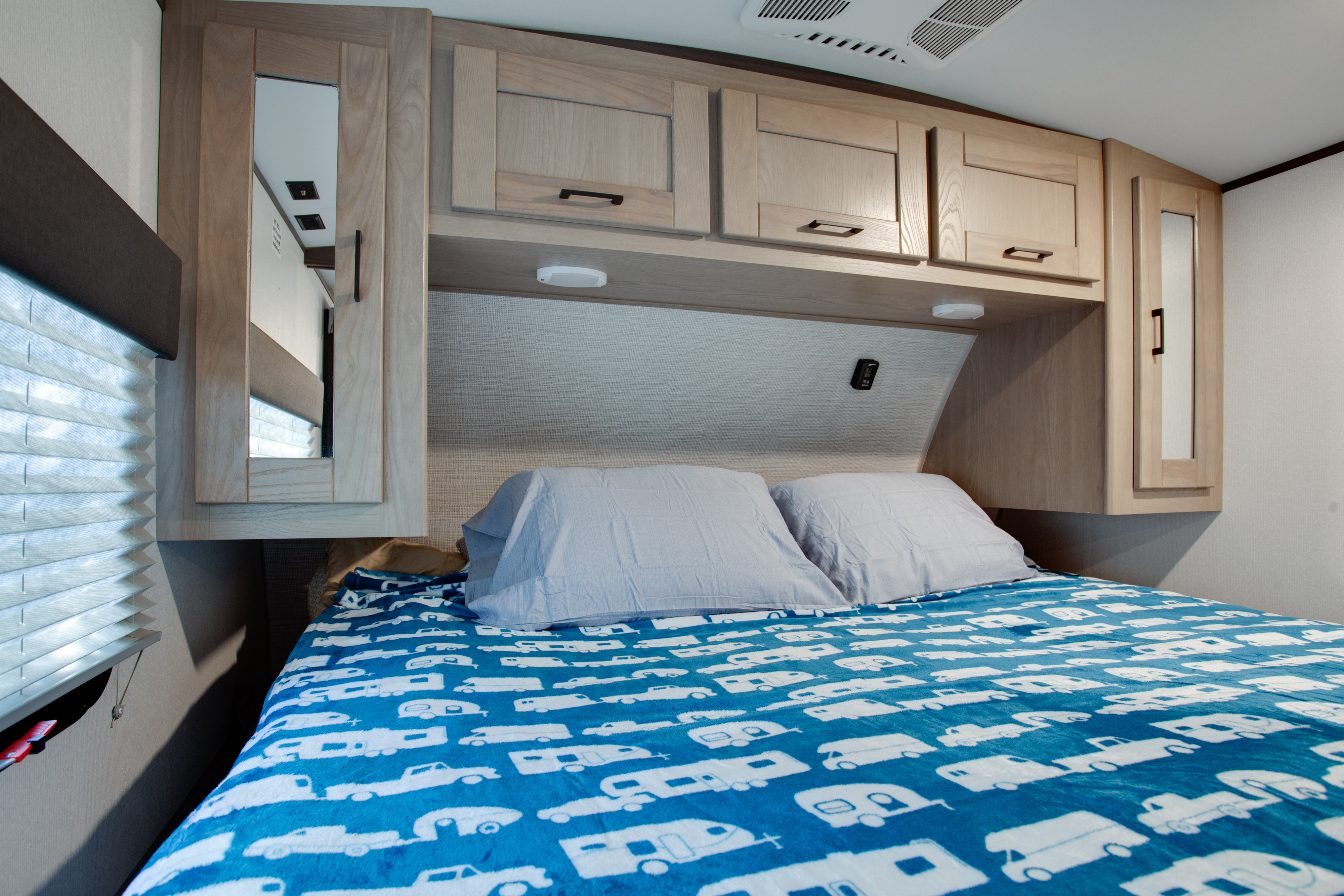 Interior of an RV rental bedroom with light wood cabinets, blue camper-themed blanket, and window.. Cruiser Rv Corp Shadow Cruiser 2021