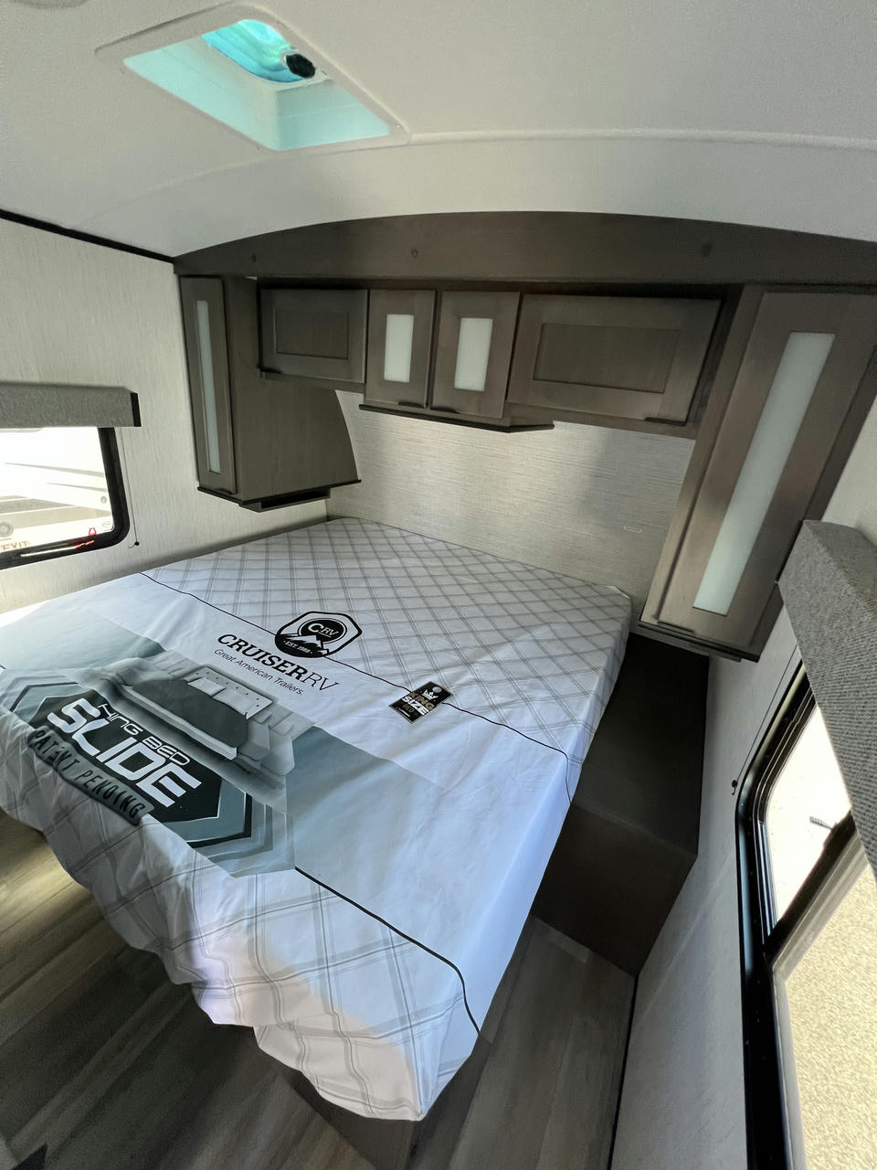 RV rental bedroom with a large bed featuring a 'Cruiser RV' cover. Dark wood overhead cabinets and a ceiling skylight are visible.. Cruiser Rv Corp MPG 2700TH 2022