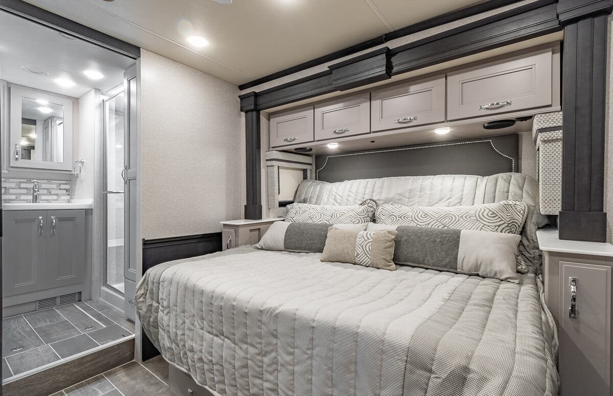 Spacious RV rental bedroom featuring a large bed, overhead storage, and an attached modern bathroom.. Thor Motor Coach Venetian 2023