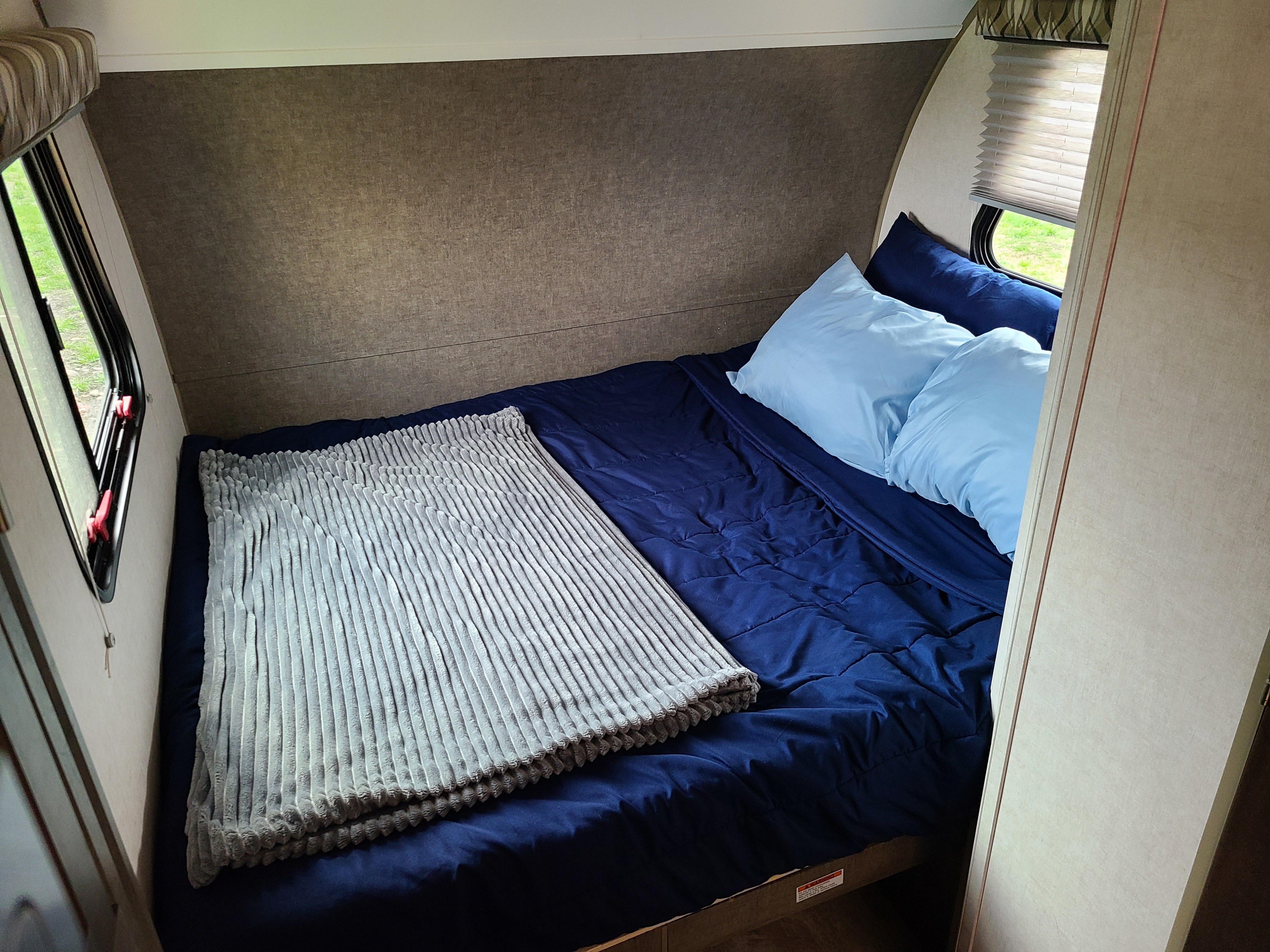 Cozy rv rental bedroom, featuring a neatly made bed with blue linens, pillows, and windows offering outdoor views.. Forest River R-Pod 2018