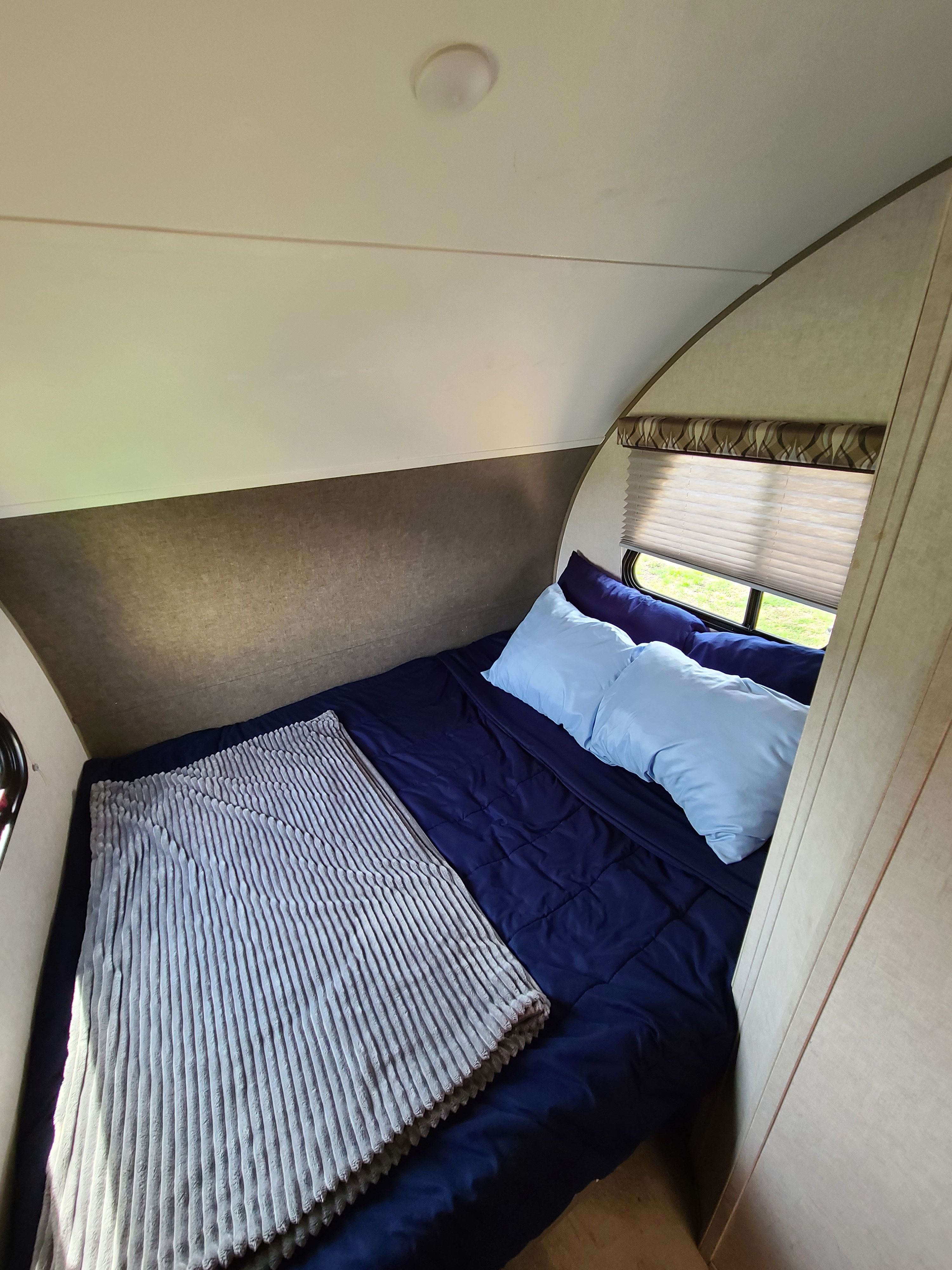 Cozy RV rental bedroom with dark blue bedding, light blue pillows, and window views. Perfect for your next trip.. Forest River R-Pod 2018