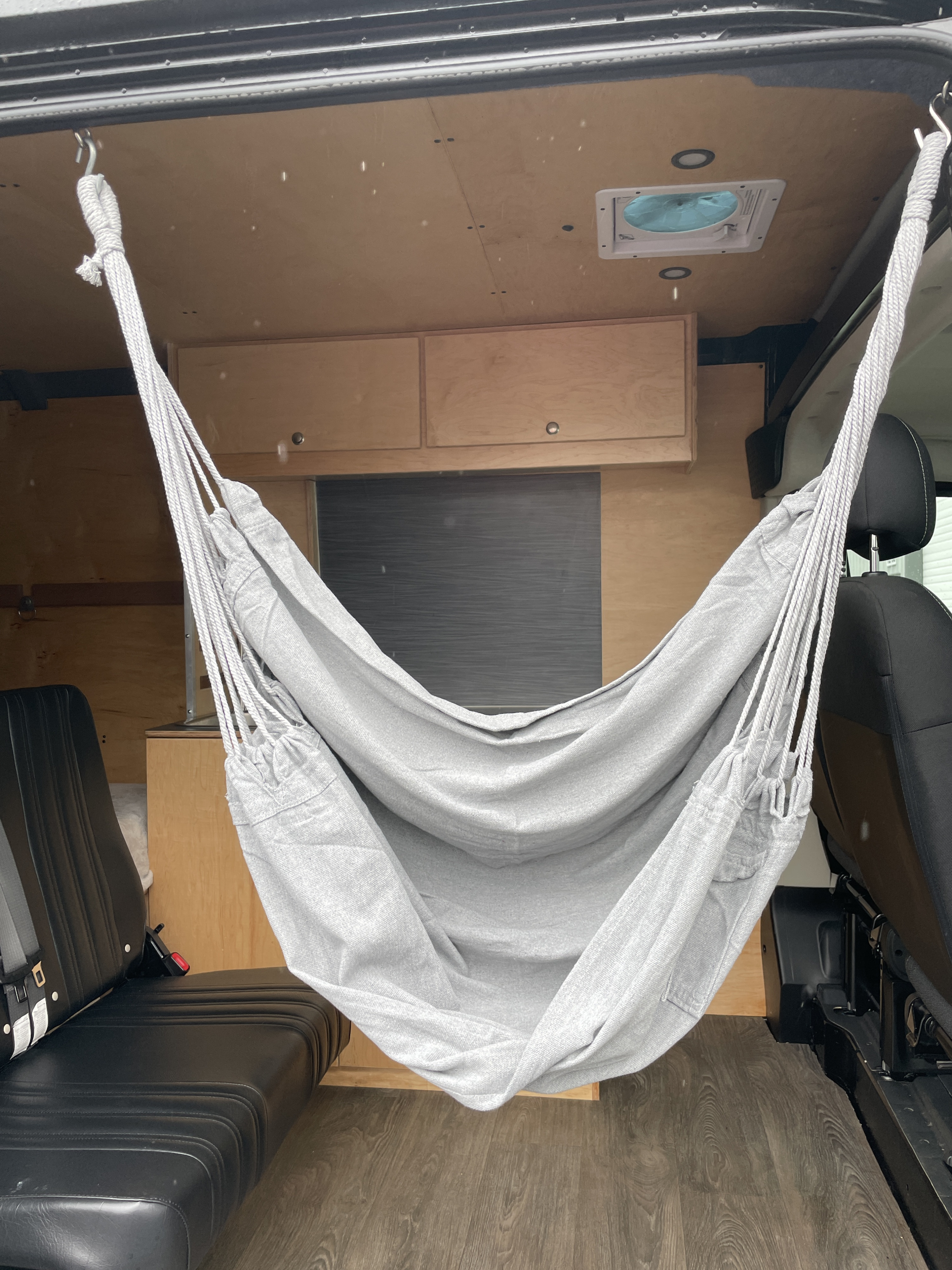 Cozy RV rental interior shows a light gray hammock, wood walls, ceiling fan, and seating, perfect for campervan trips.. RAM ProMaster 2023
