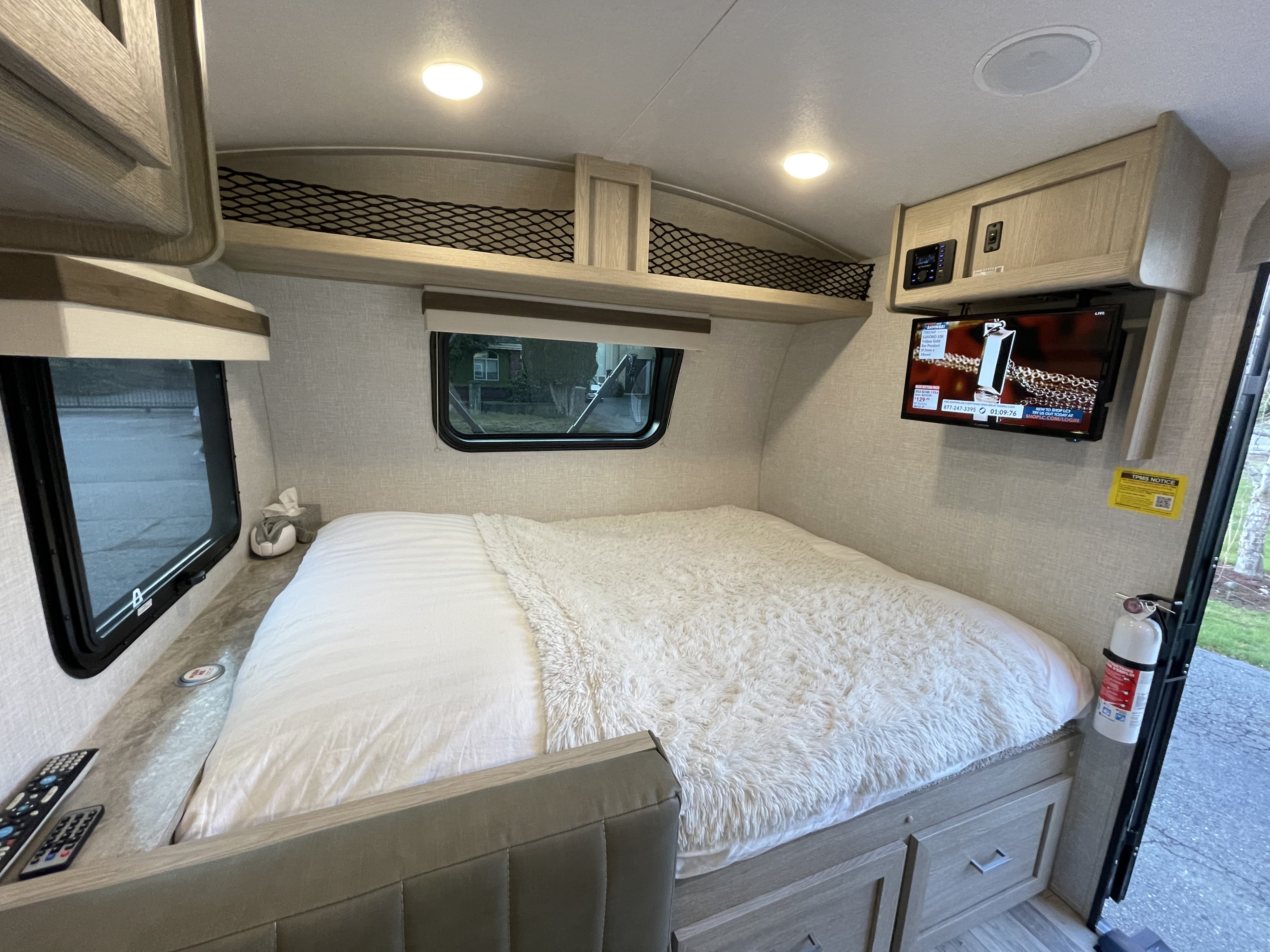 Cozy RV rental bedroom featuring a large bed with plush blanket, TV, windows, and overhead storage.. Forest River Rockwood Geo Pro 2022