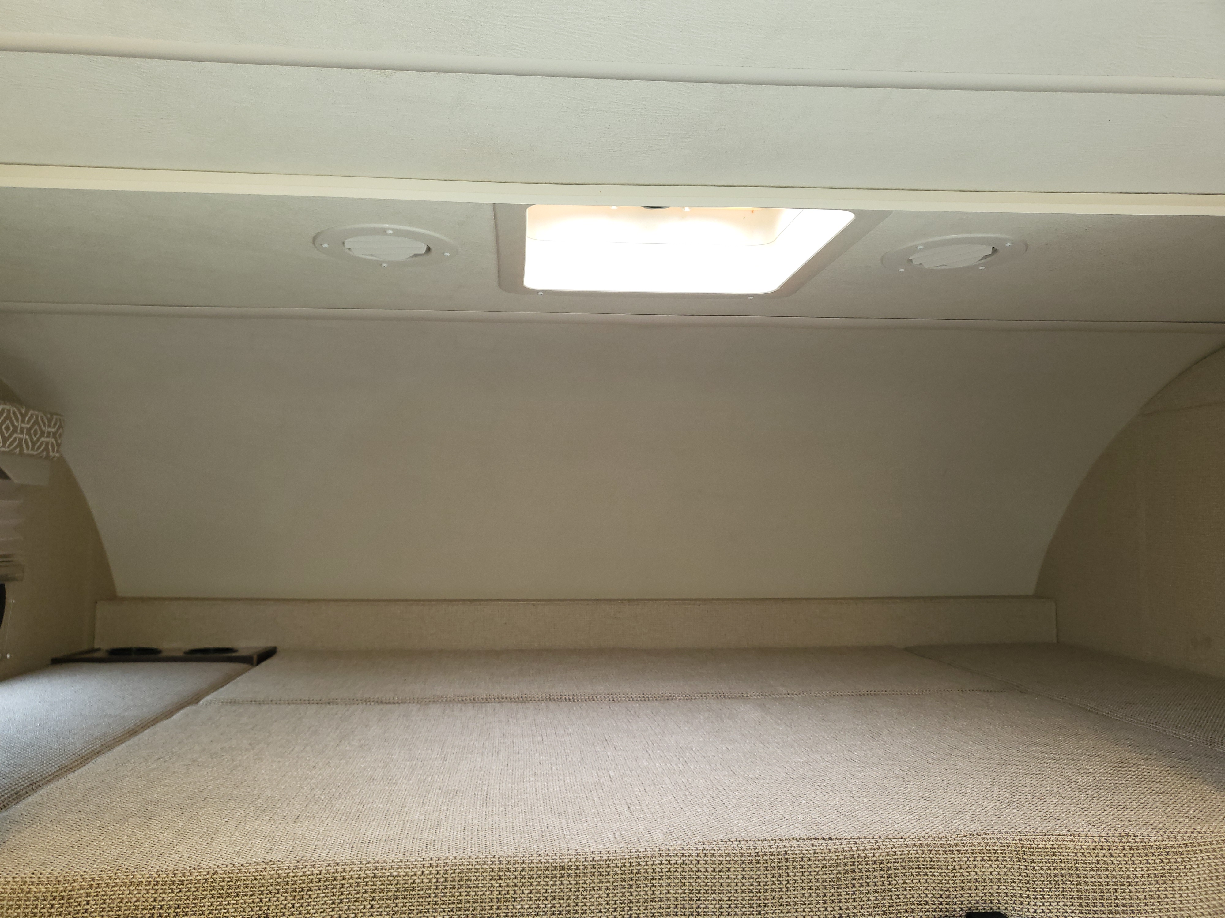 The over-cab bunk area of an RV rental, featuring a textured mattress, ceiling light, and two round vents.. Thor Freedom Elite 2018