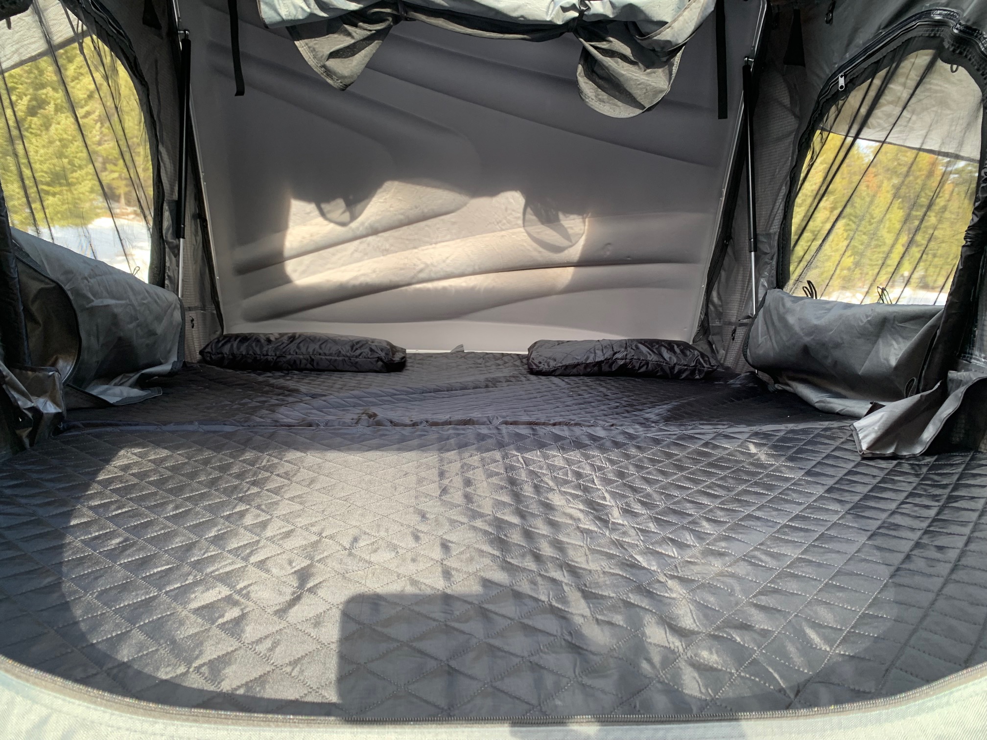 Cozy interior of an RV rental rooftop tent, with a quilted mattress and scenic outdoor views for camping.. Toyota Toyota Land Cruiser 1995