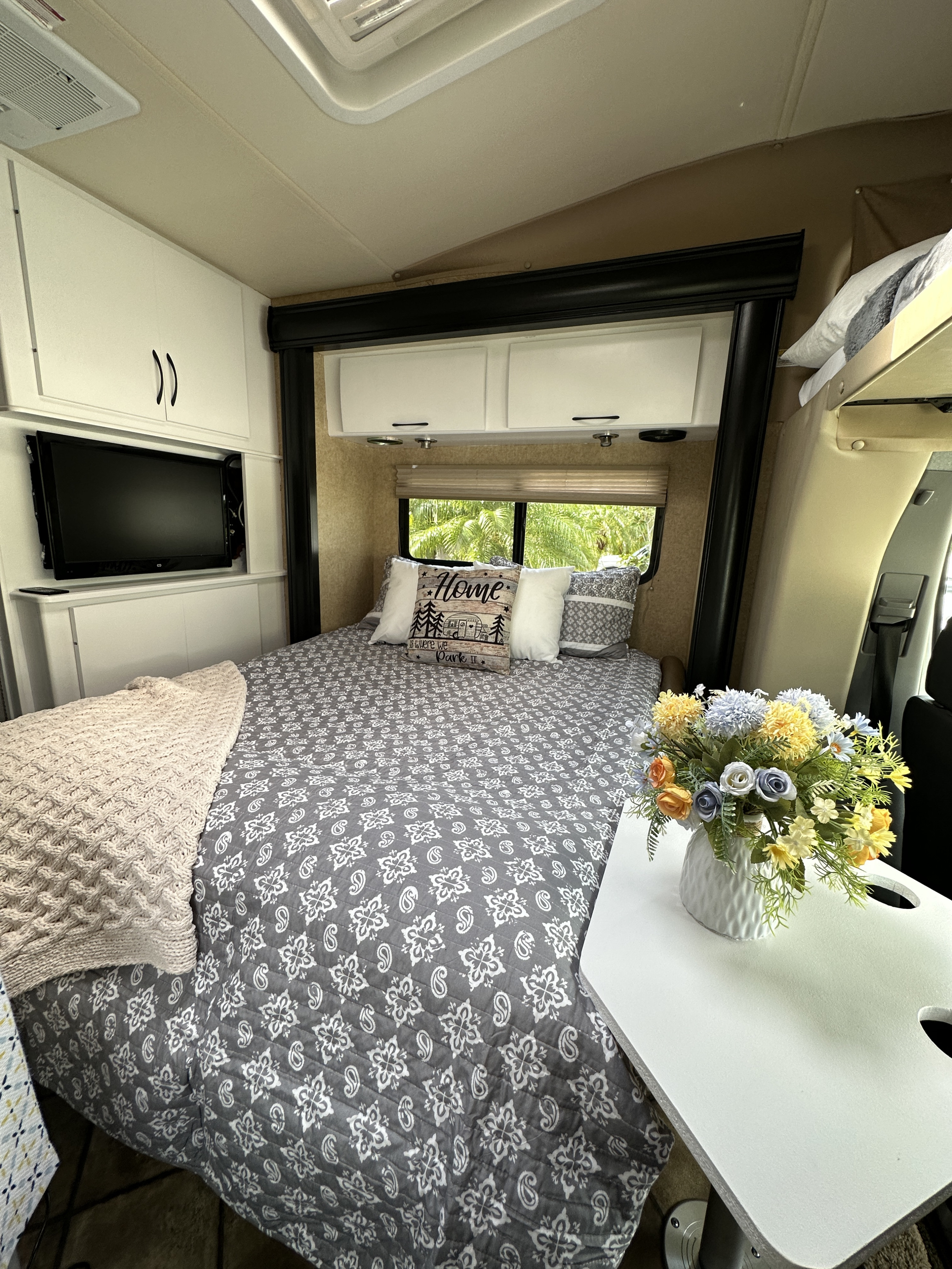 Inside this cozy rv rental: a compact bedroom with patterned bed, TV, overhead storage, and a vibrant floral centerpiece.. Thor Four Winds Siesta 2014
