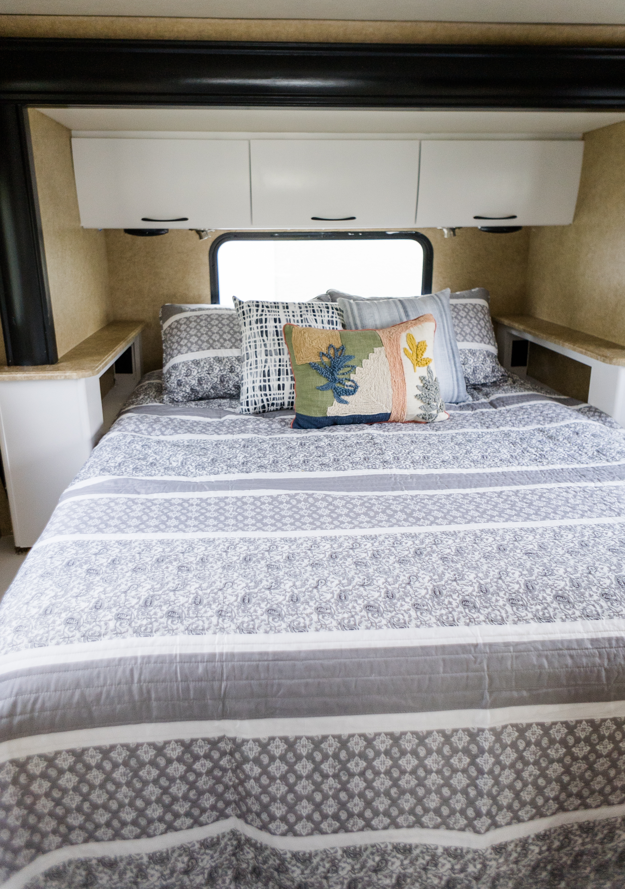 Comfortable RV rental sleeping area with grey and white patterned bedding, colorful pillows, and cabinets above.. Thor Four Winds Siesta 2014