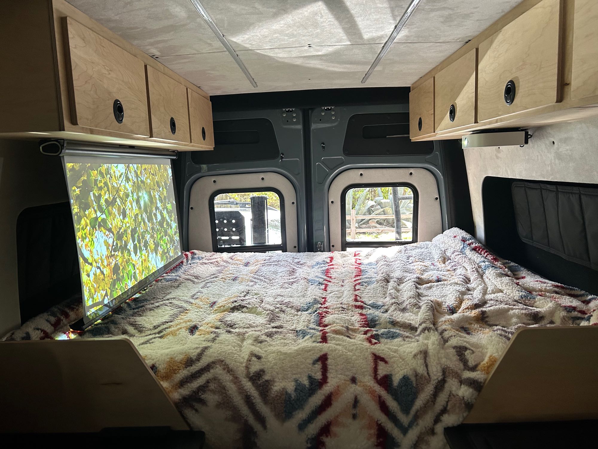 Cozy RV rental interior with a built-in projector screen over the comfortable bed and ample overhead storage.. Mercedes-Benz Sprinter RV Motorhome Campervan 2022