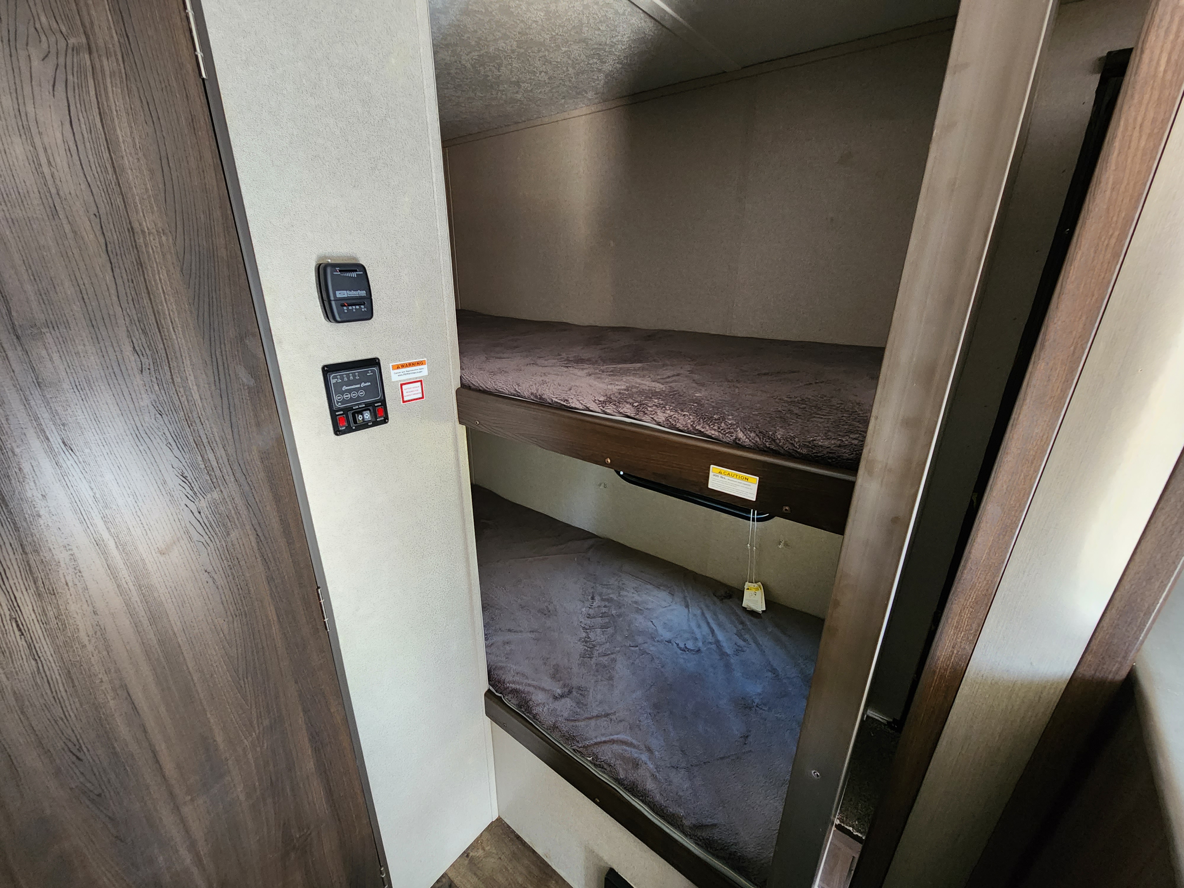 Inside an RV rental: two bunk beds with dark bedding, and vehicle control panels on the wall. A compact sleeping space.. Keystone RV Springdale 2019