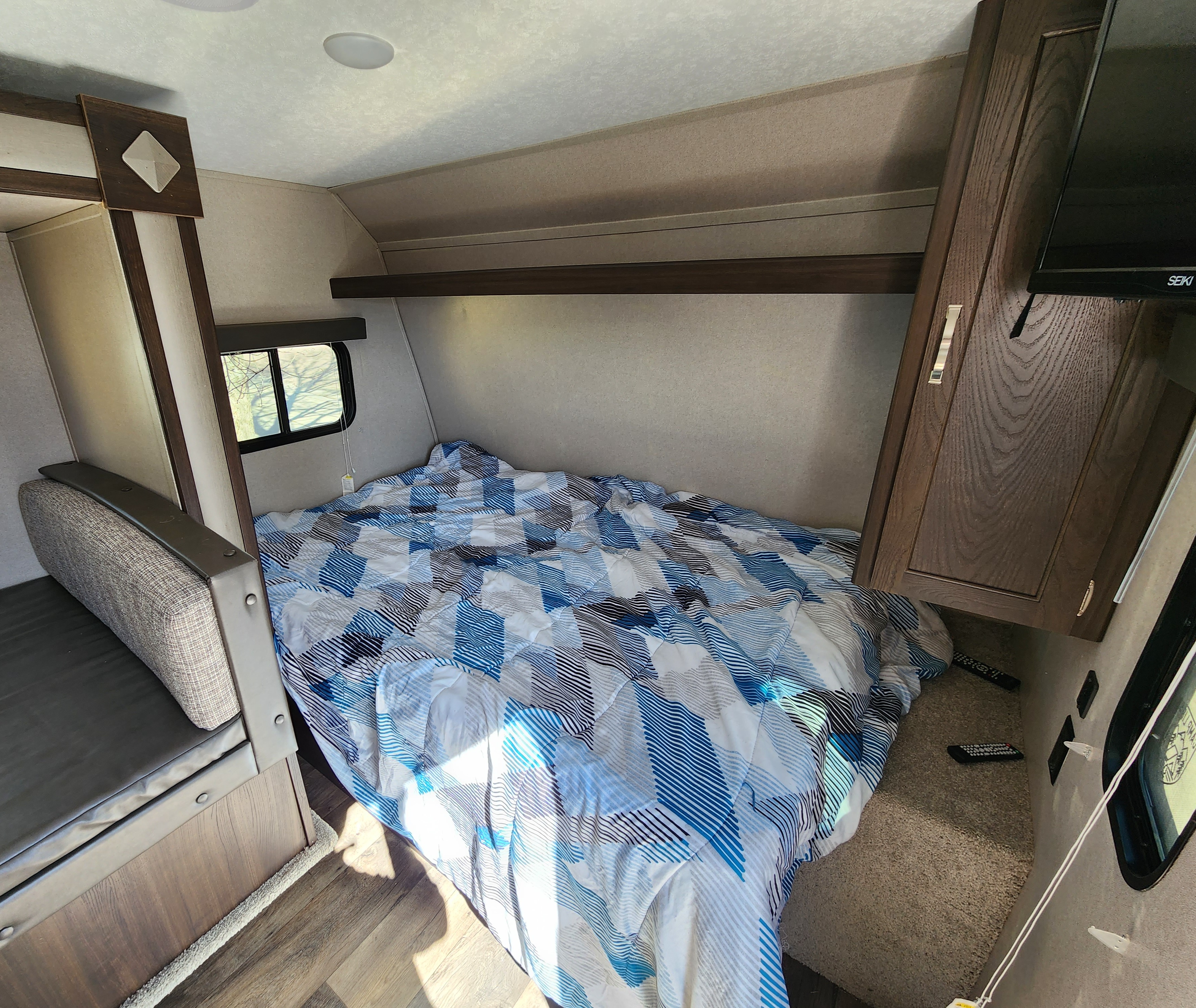 RV rental bedroom with blue patterned bed, compact seating, mounted TV, and overhead storage, ideal for travel.. Keystone RV Springdale 2019