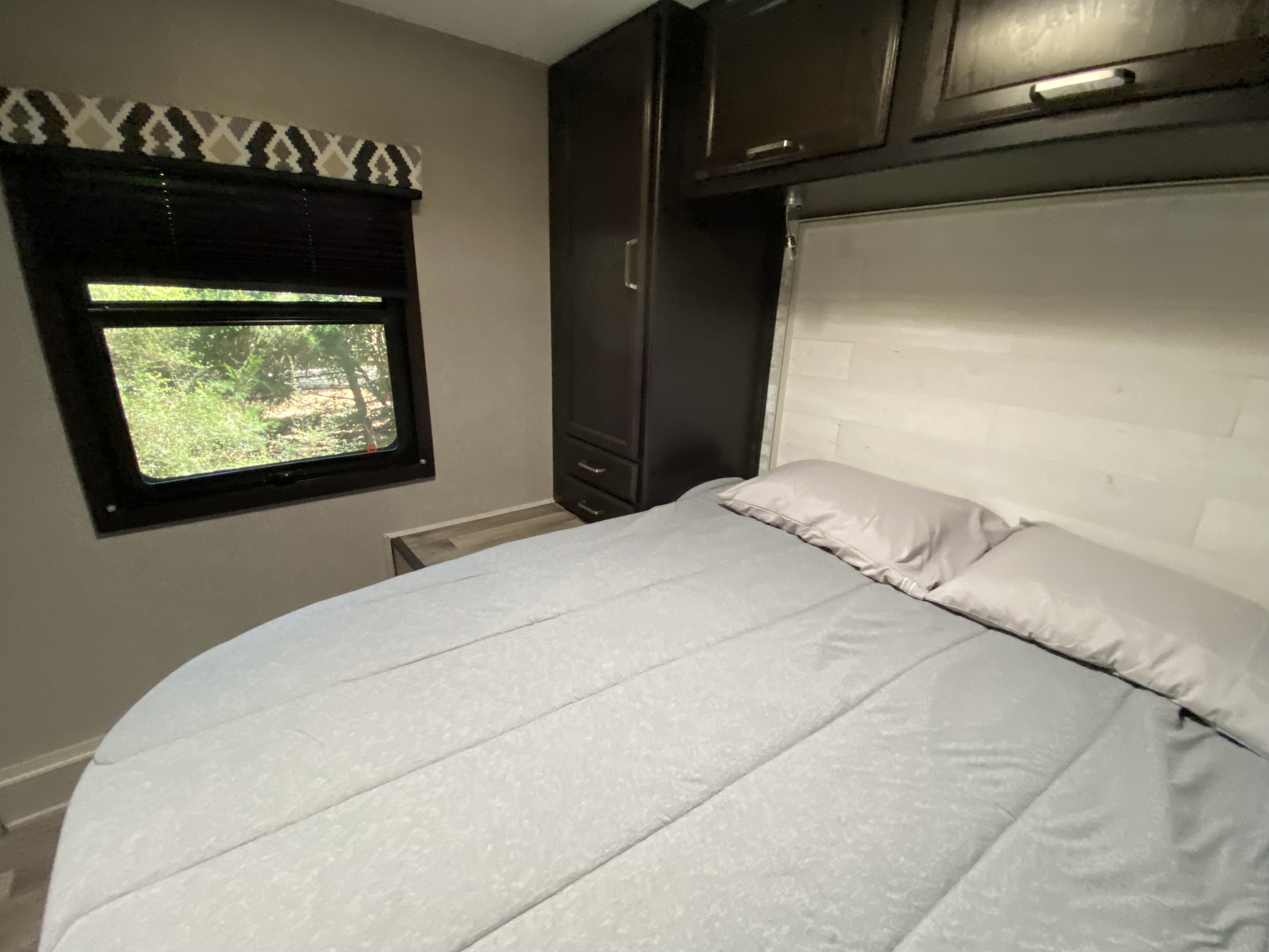 Inside a comfortable RV rental bedroom featuring a bed, window with nature views, and functional cabinetry.. Jayco Redhawk 2021