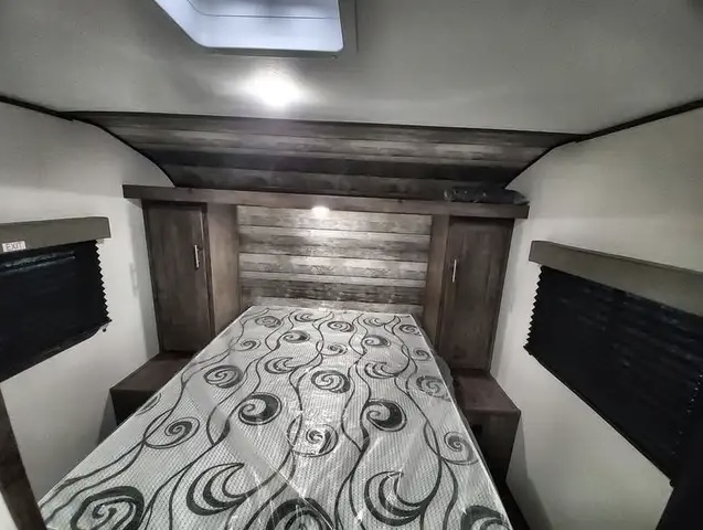 RV rental bedroom with a comfortable queen bed (still wrapped), wood headboard, and built-in storage.. Riverside Rv Retro 2022