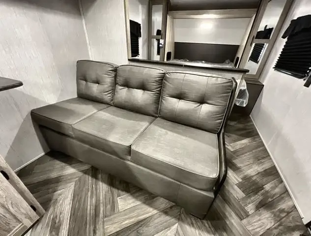 Modern grey sofa bed in a compact RV rental living area, featuring herringbone flooring and a cozy bunk. Perfect for travel.. Heartland Prowler 2023