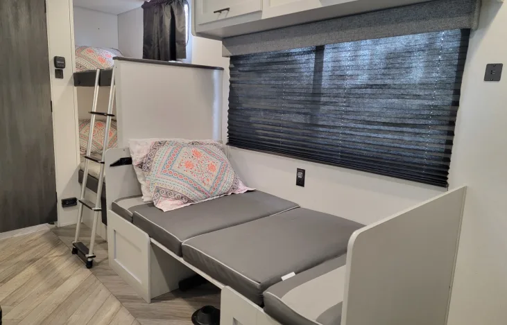 RV rental bunkhouse: features bunk beds with ladder, and a grey cushioned daybed by a window with blinds.. Forest River Salem FSX 2021