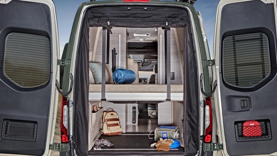 Rear view of an RV rental camper van, doors open, revealing a multi-level interior with bed, organized storage, and gear.. Mercedes-Benz Entegra Launch 2023