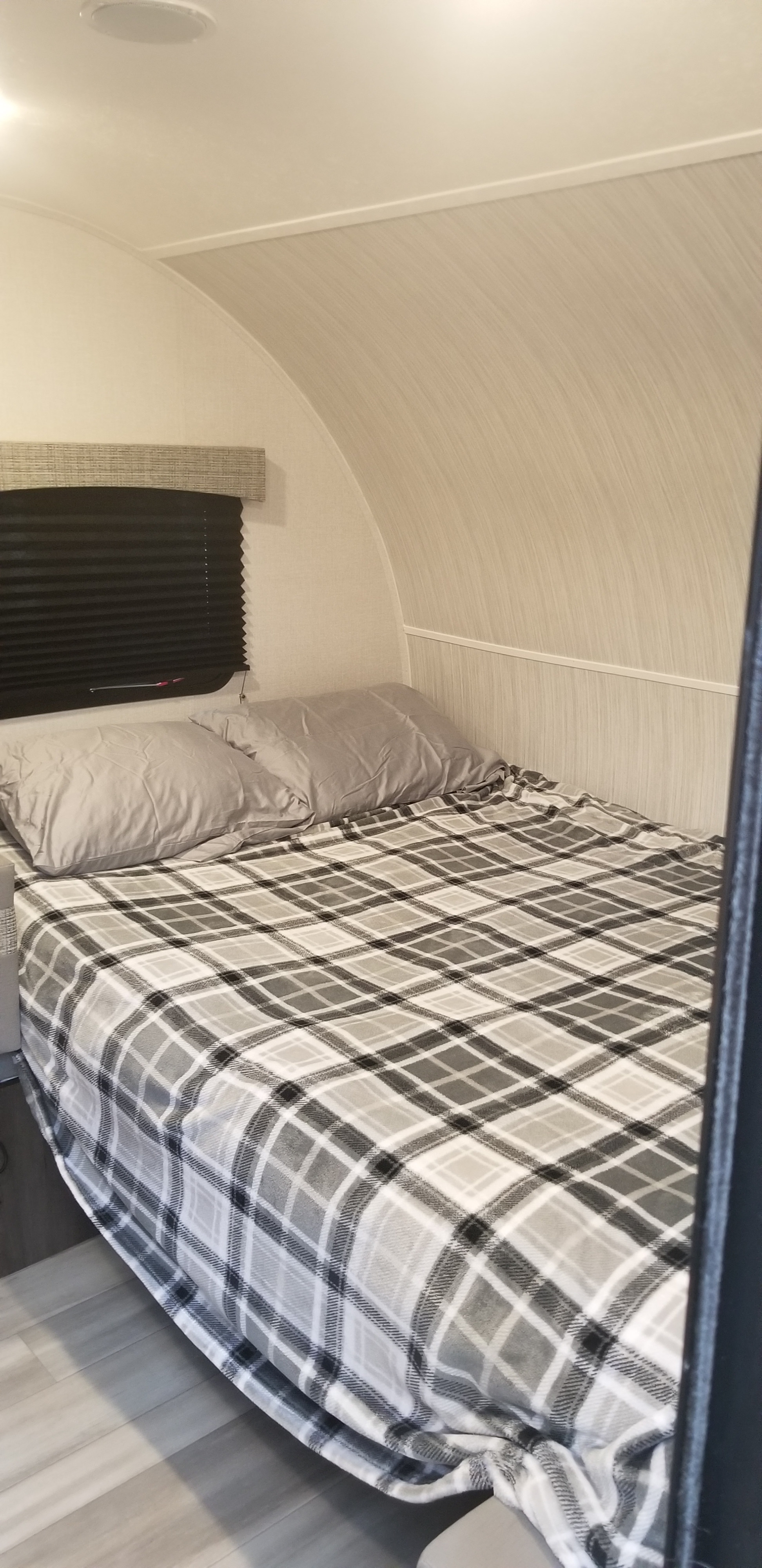 RV rental bedroom featuring a full bed with a grey and white plaid blanket, light grey pillows, and a pleated window blind.. Coachmen Clipper 2022