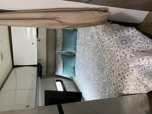 Comfortable RV rental bedroom with patterned bedding, teal pillows, and sleek overhead storage.. Winnebago View 2020